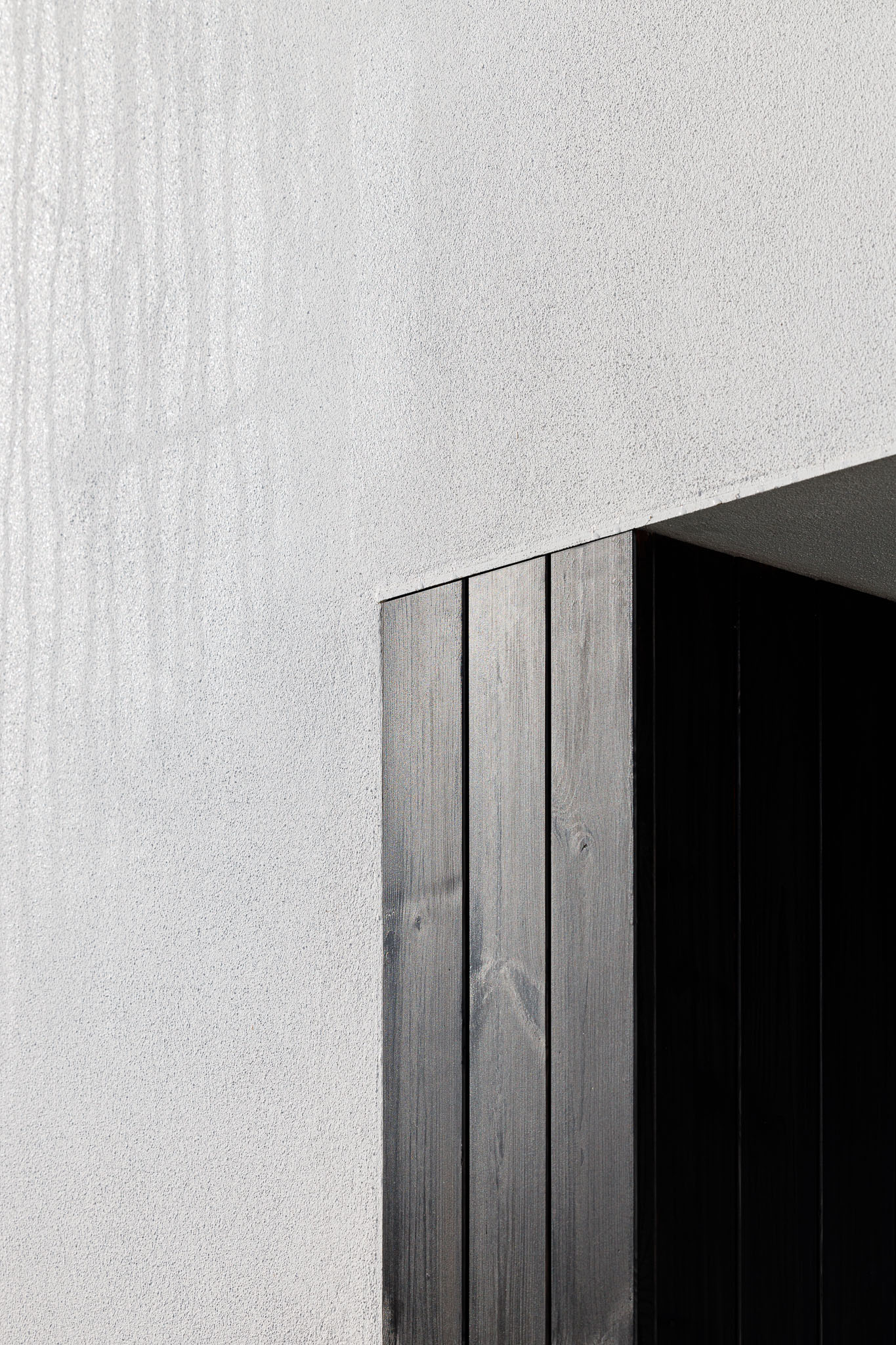 Detalhe de entrada com revestimento em madeira escura contrastando com a parede branca texturada. — Habitação em Santa Joana arquitetura Nu.ma em Aveiro