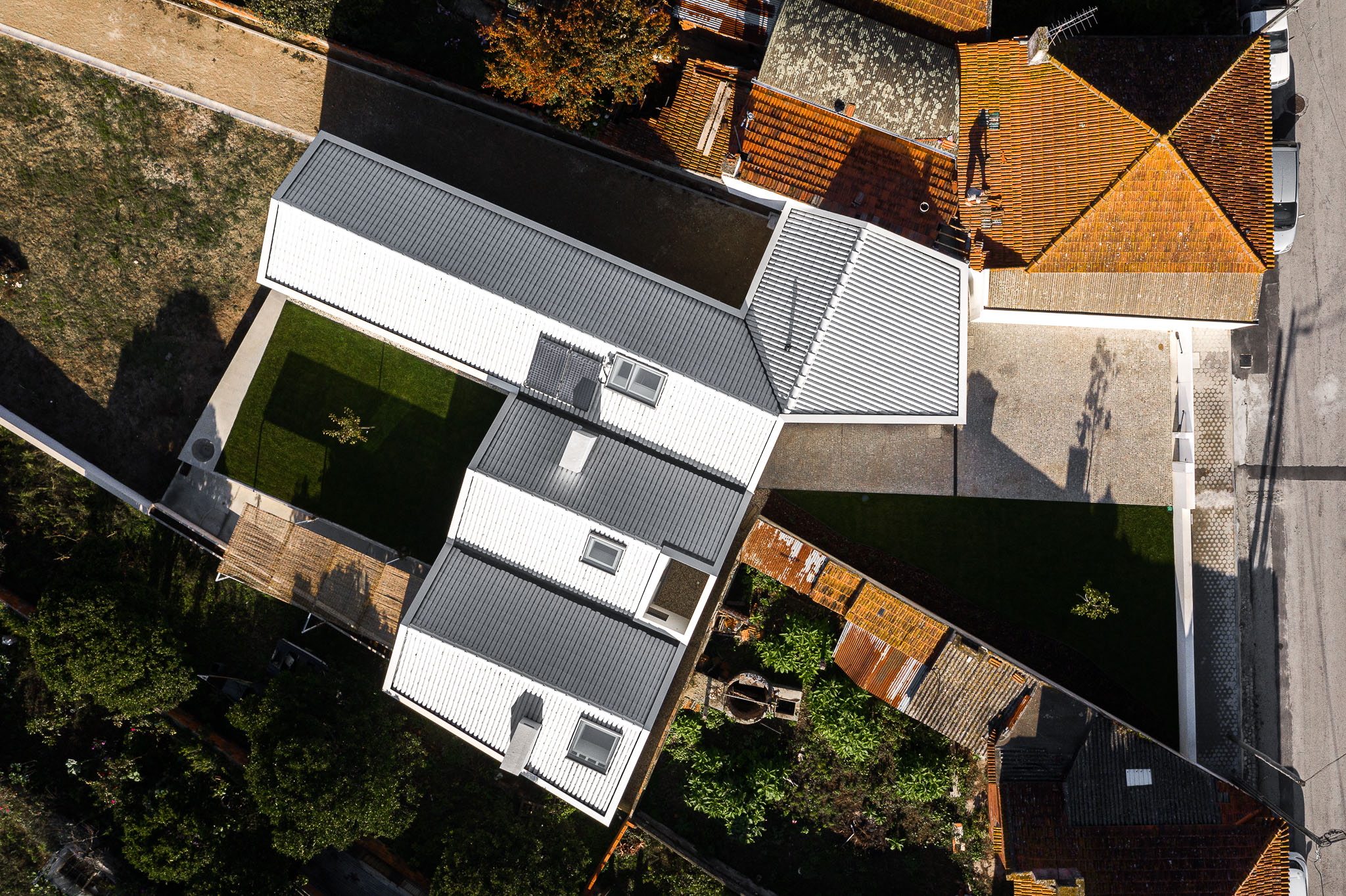 Vista aérea da casa com telhado metálico, pátios relvados e integração no tecido urbano existente. — Habitação em Santa Joana arquitetura Nu.ma em Aveiro