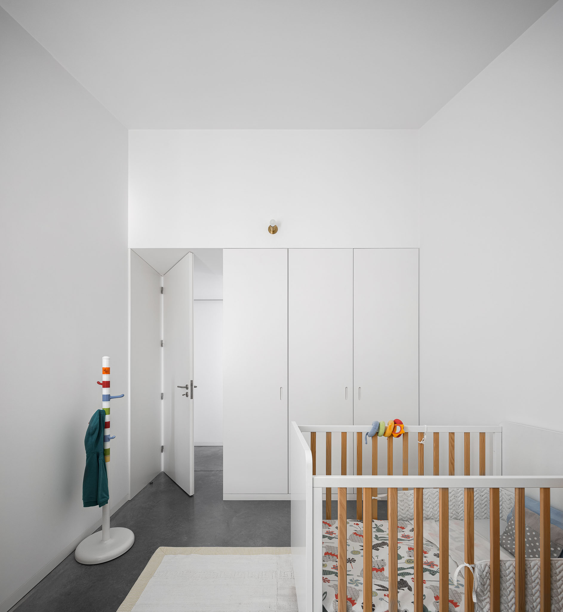 Quarto infantil com berço de madeira clara, armário branco embutido e pavimento em betão cinzento. — Habitação em Santa Joana arquitetura Nu.ma em Aveiro