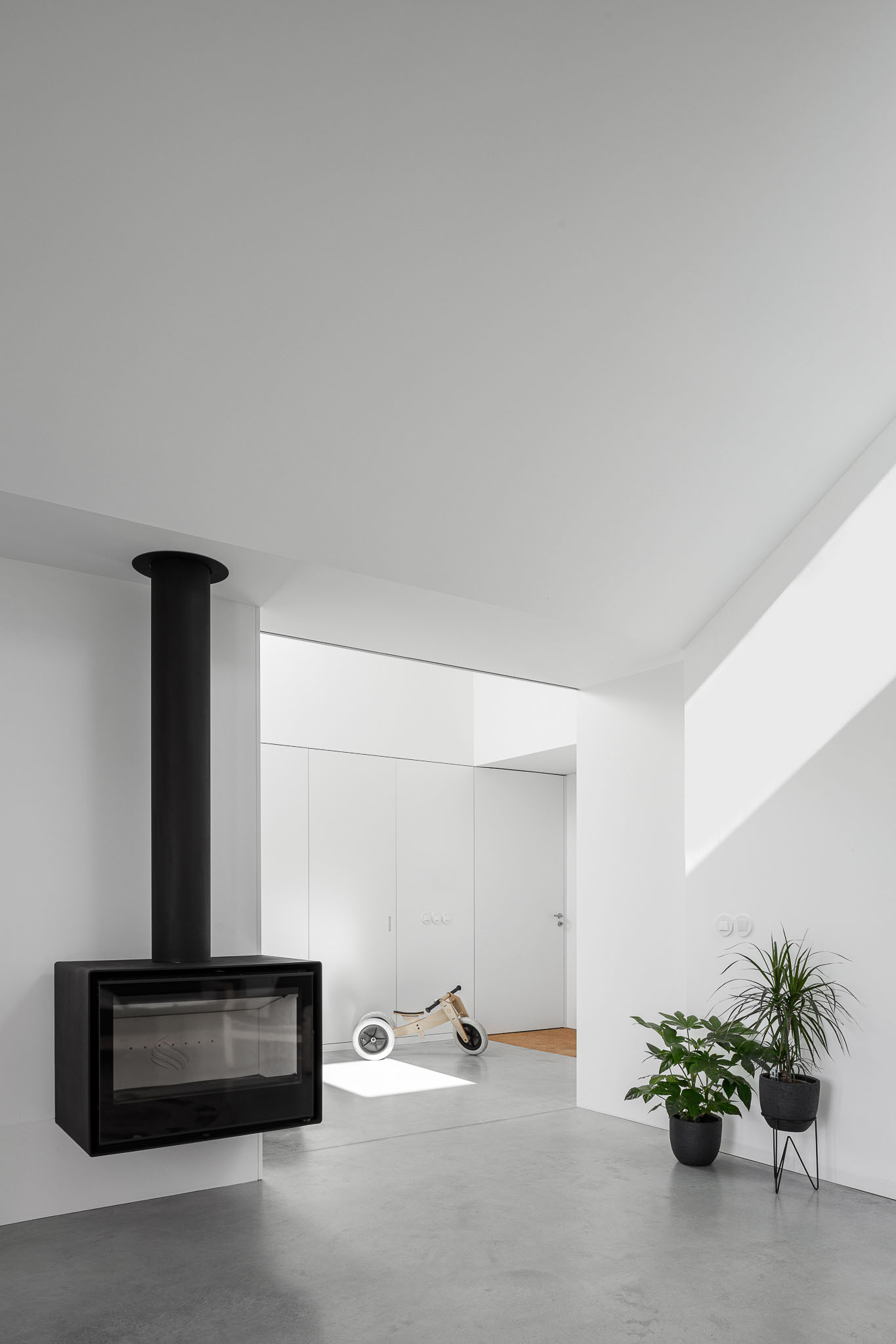 Sala de estar com lareira suspensa preta, pavimento em betão polido e iluminação natural zenital. — Habitação em Santa Joana arquitetura Nu.ma em Aveiro