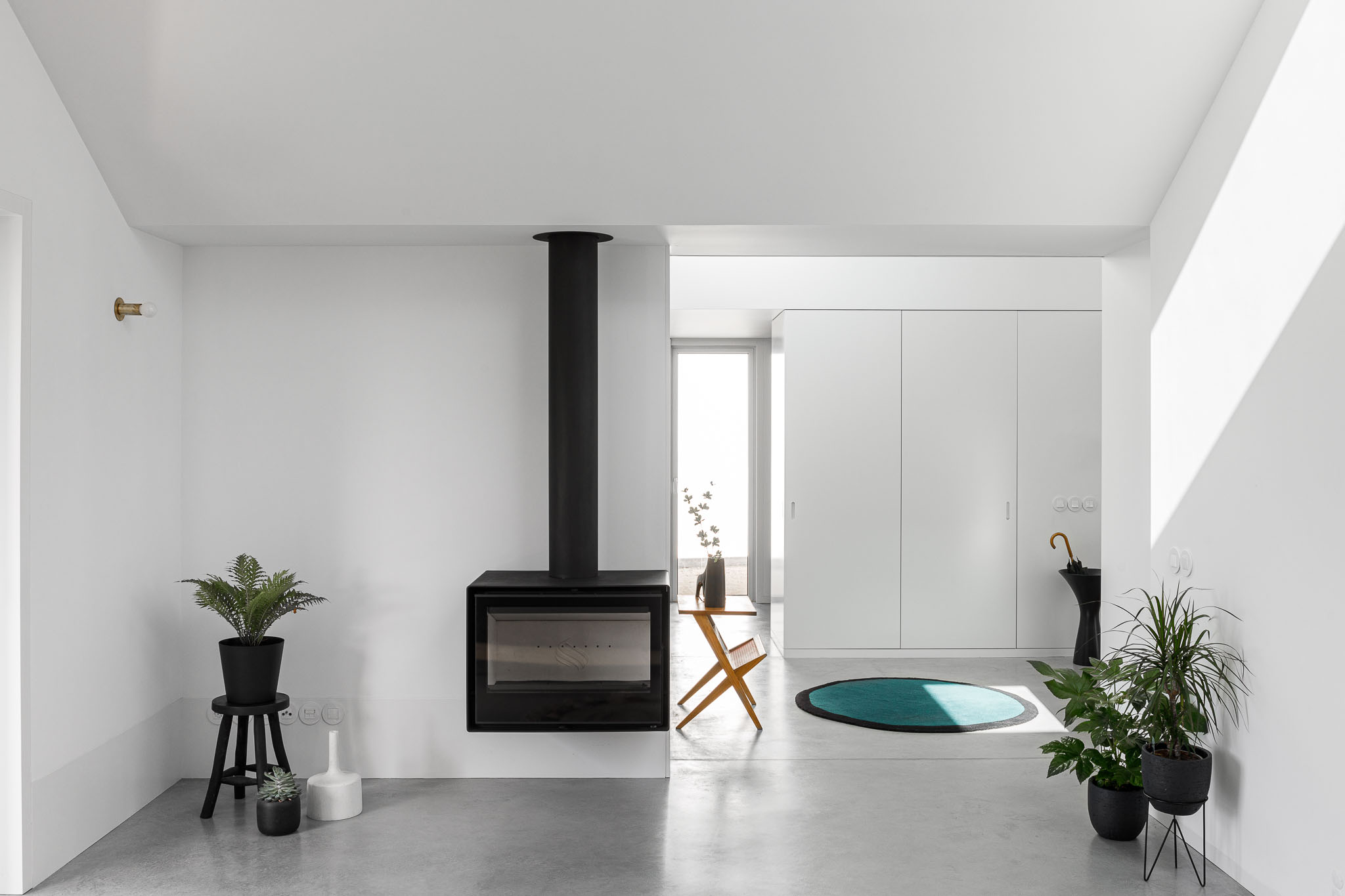 Sala de estar com lareira, mobiliário minimalista, pavimento em betão polido e plantas decorativas. — Habitação em Santa Joana arquitetura Nu.ma em Aveiro