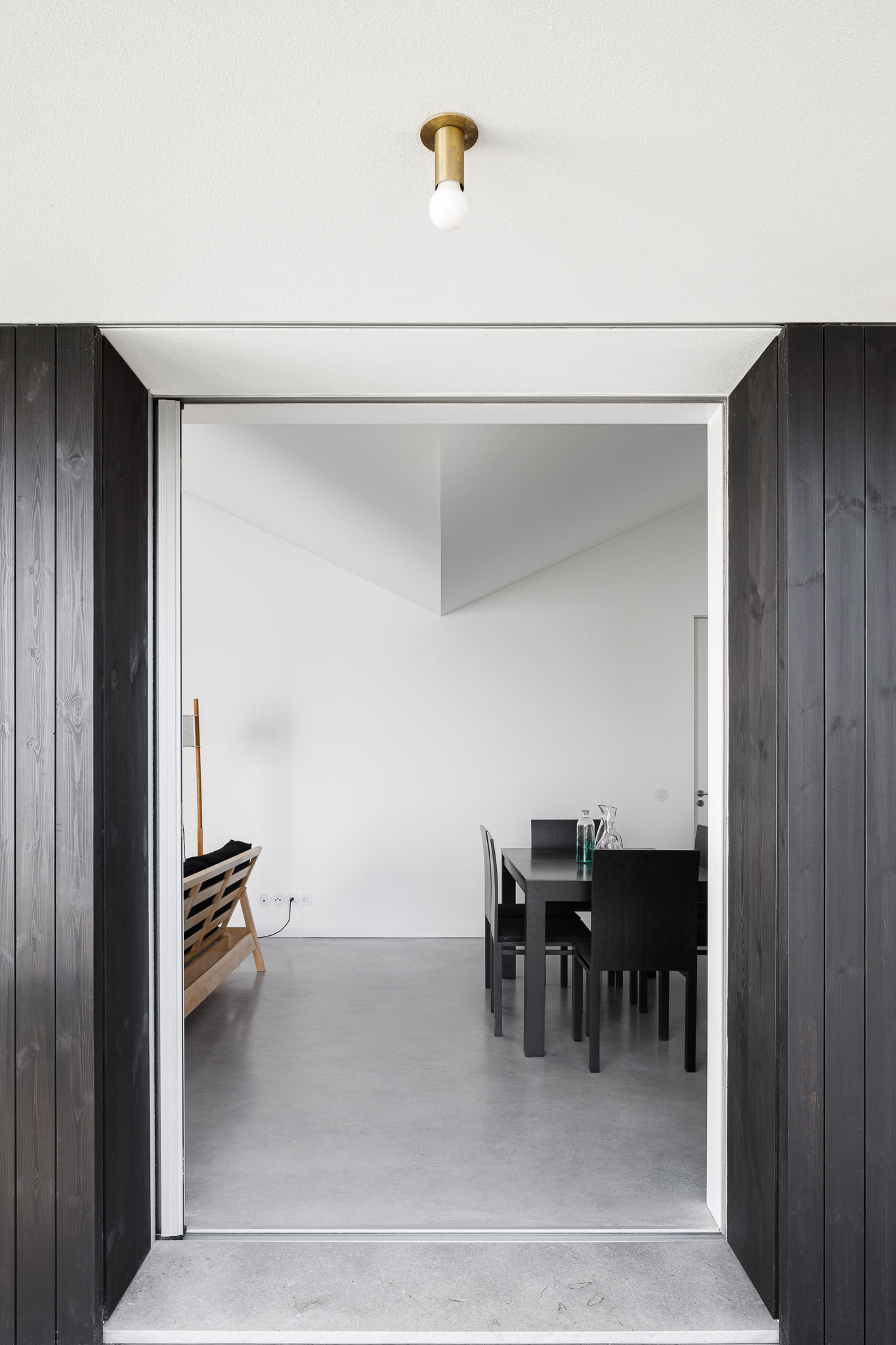 Perspectiva de porta com moldura em madeira escura, revelando sala de jantar com mobiliário preto e branco. — Habitação em Santa Joana arquitetura Nu.ma em Aveiro