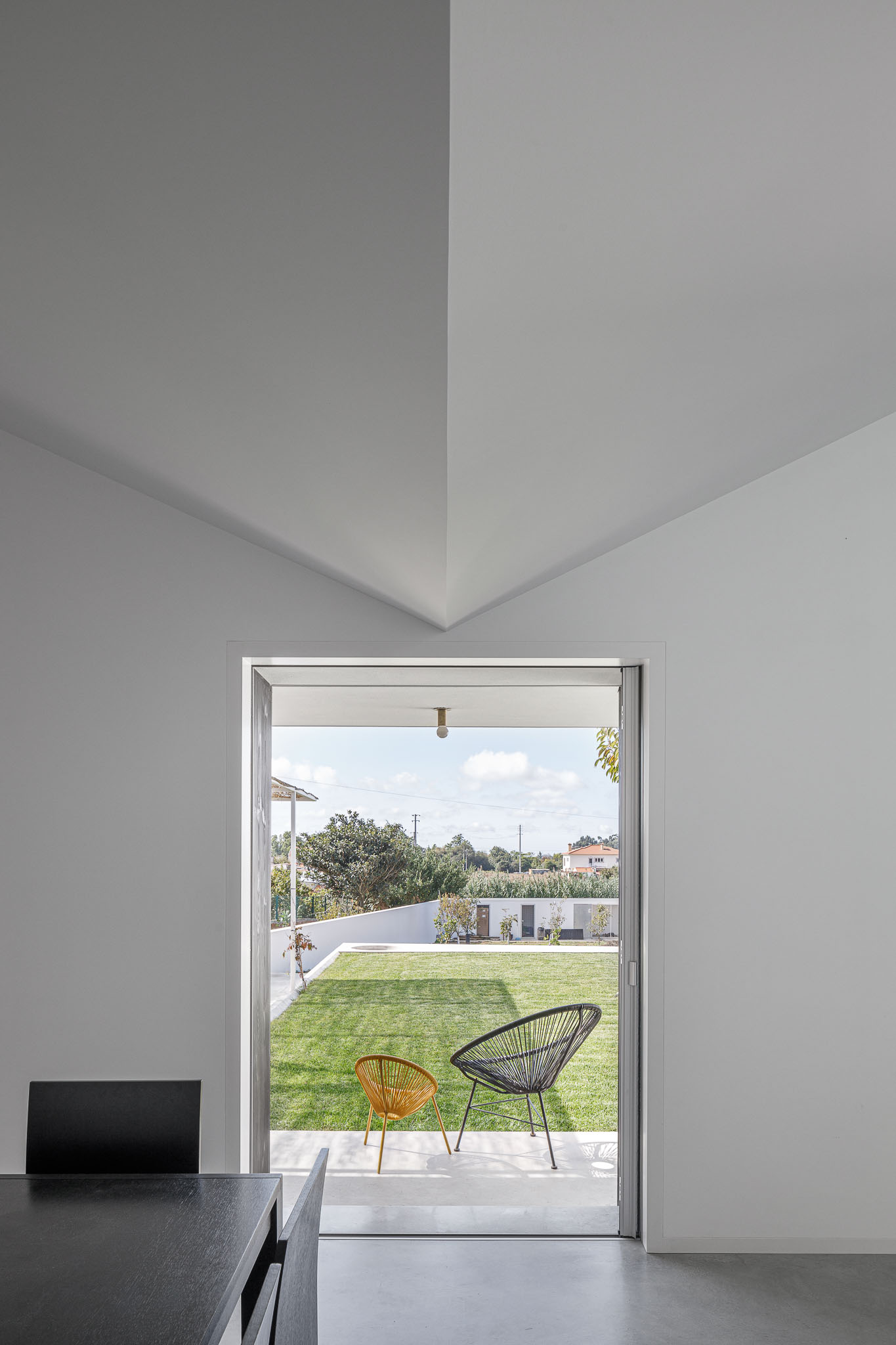 Vista da sala de jantar para o jardim, com cadeiras de design e pavimento contínuo em betão. — Habitação em Santa Joana arquitetura Nu.ma em Aveiro