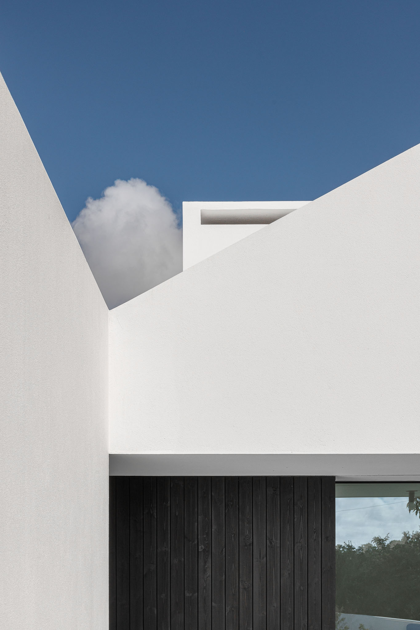 Composição de volumes brancos com telhados inclinados e revestimento em madeira escura, sob céu azul. — Habitação em Santa Joana arquitetura Nu.ma em Aveiro