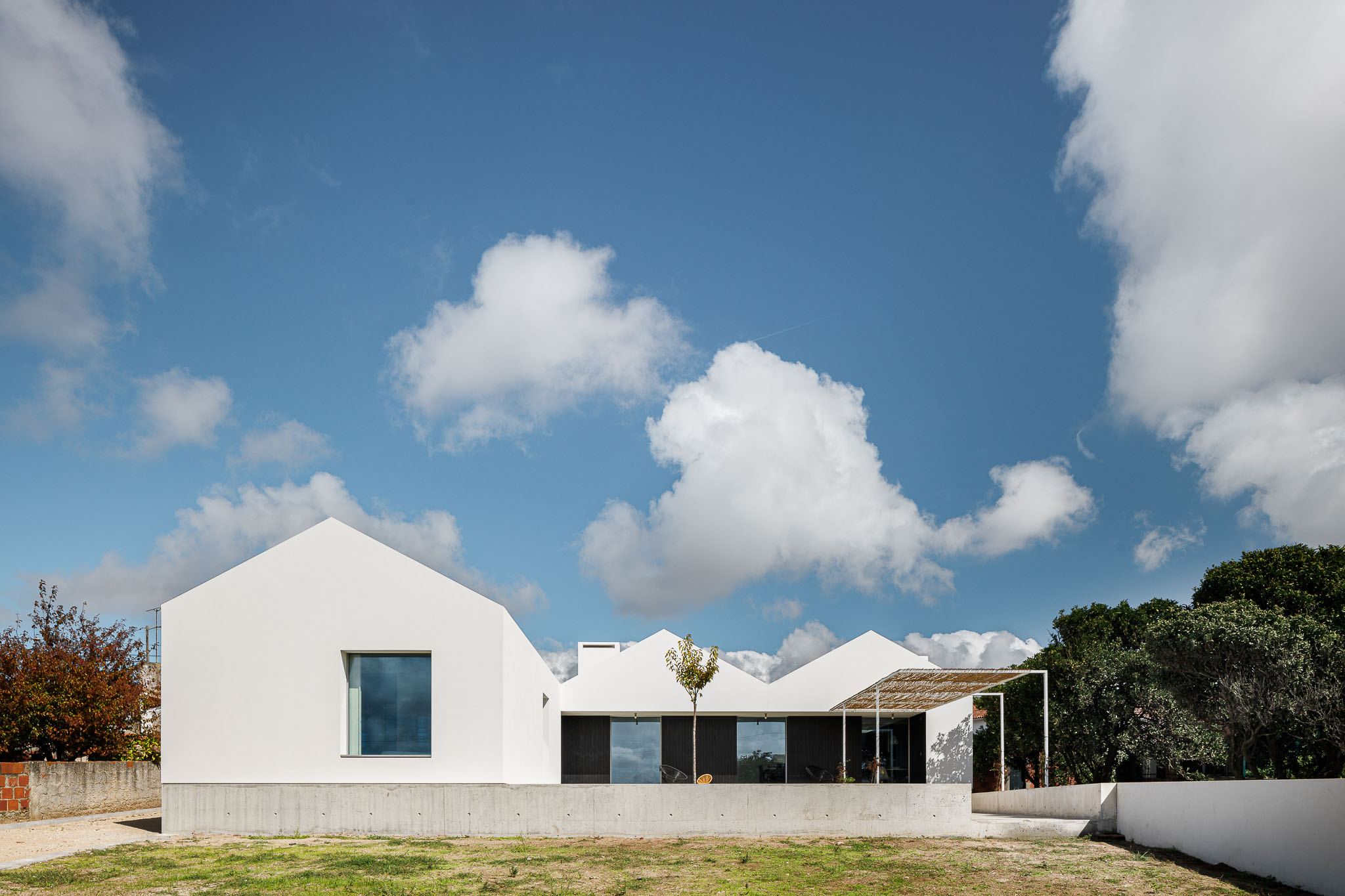 Vista frontal da casa com volumes brancos, telhados inclinados e alpendre com cobertura natural. — Habitação em Santa Joana arquitetura Nu.ma em Aveiro