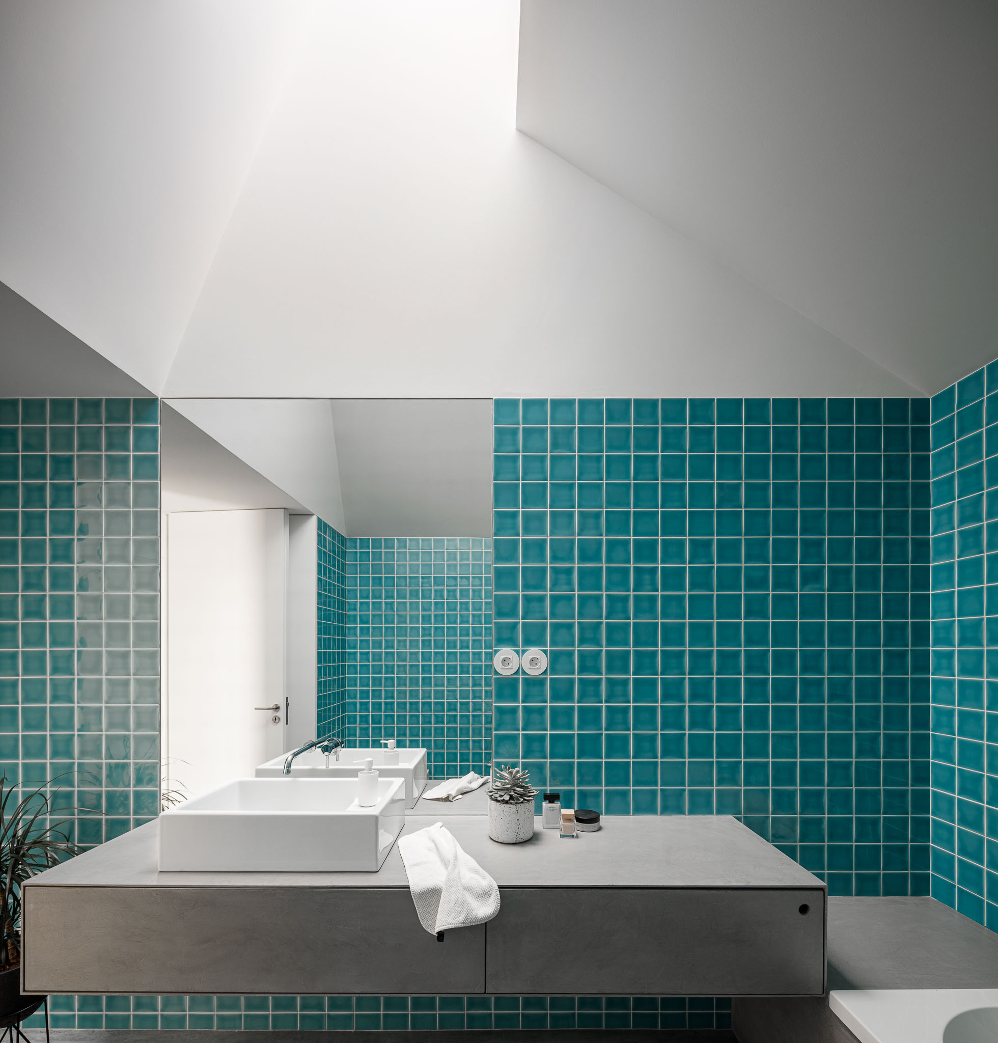 Casa de banho com azulejos turquesa, lavatório branco sobre móvel de betão e luz zenital. — Habitação em Santa Joana arquitetura Nu.ma em Aveiro