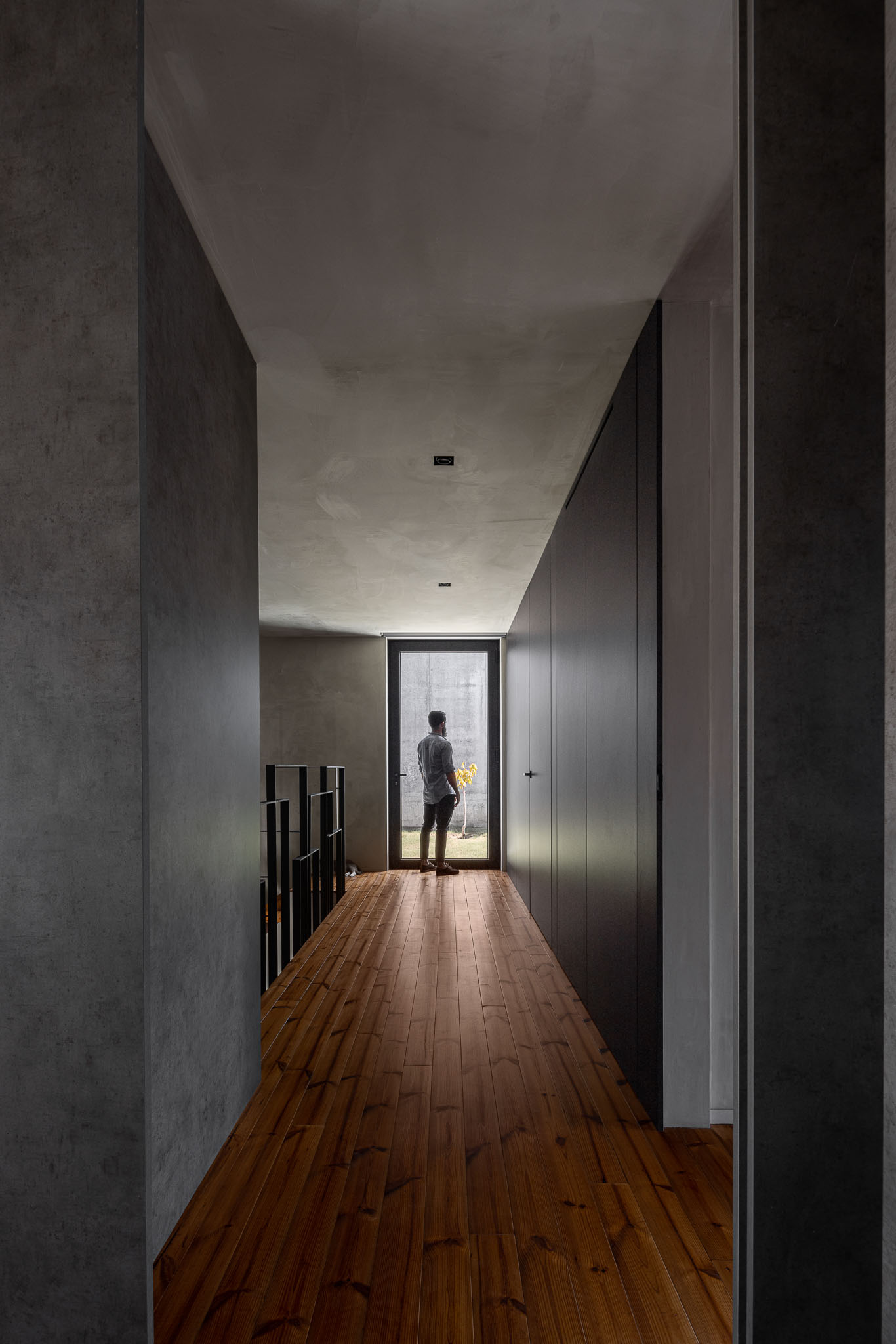 Corredor interior com pavimento em madeira, paredes cinzentas e porta envidraçada ao fundo. — Casa 15 arquitetura AM-arqstudio em Braga