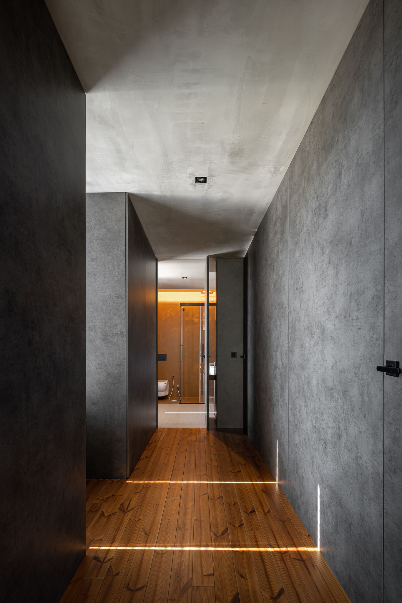 Corredor com chão em madeira, paredes texturadas cinzentas e iluminação embutida no chão. — Casa 15 arquitetura AM-arqstudio em Braga