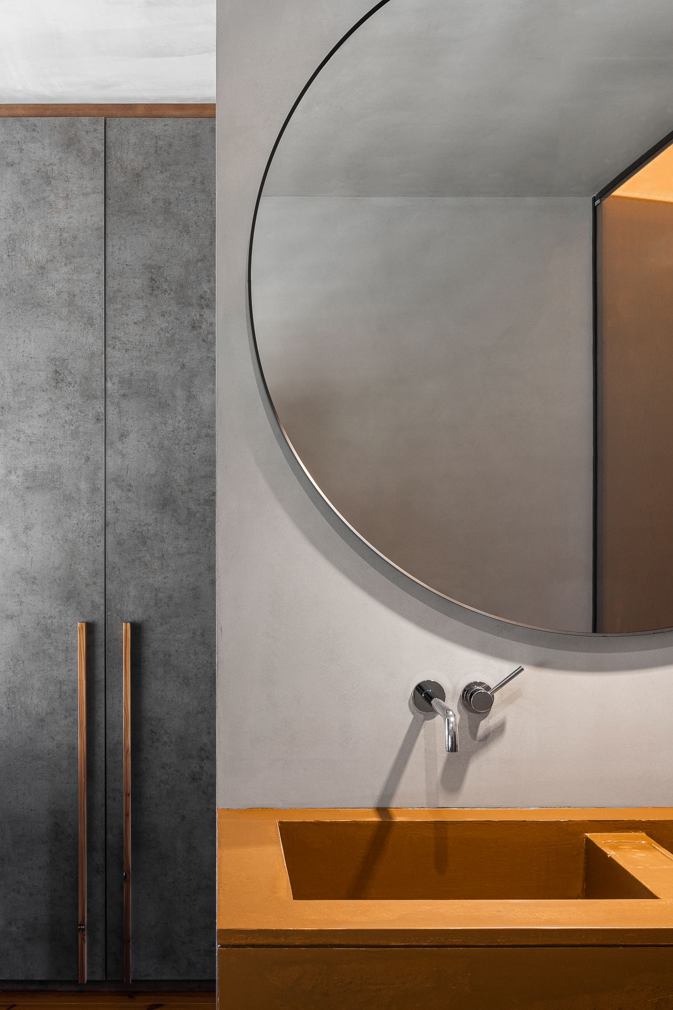 Detalhe de lavatório em madeira com espelho circular e armário cinzento com puxadores metálicos. — Casa 15 arquitetura AM-arqstudio em Braga