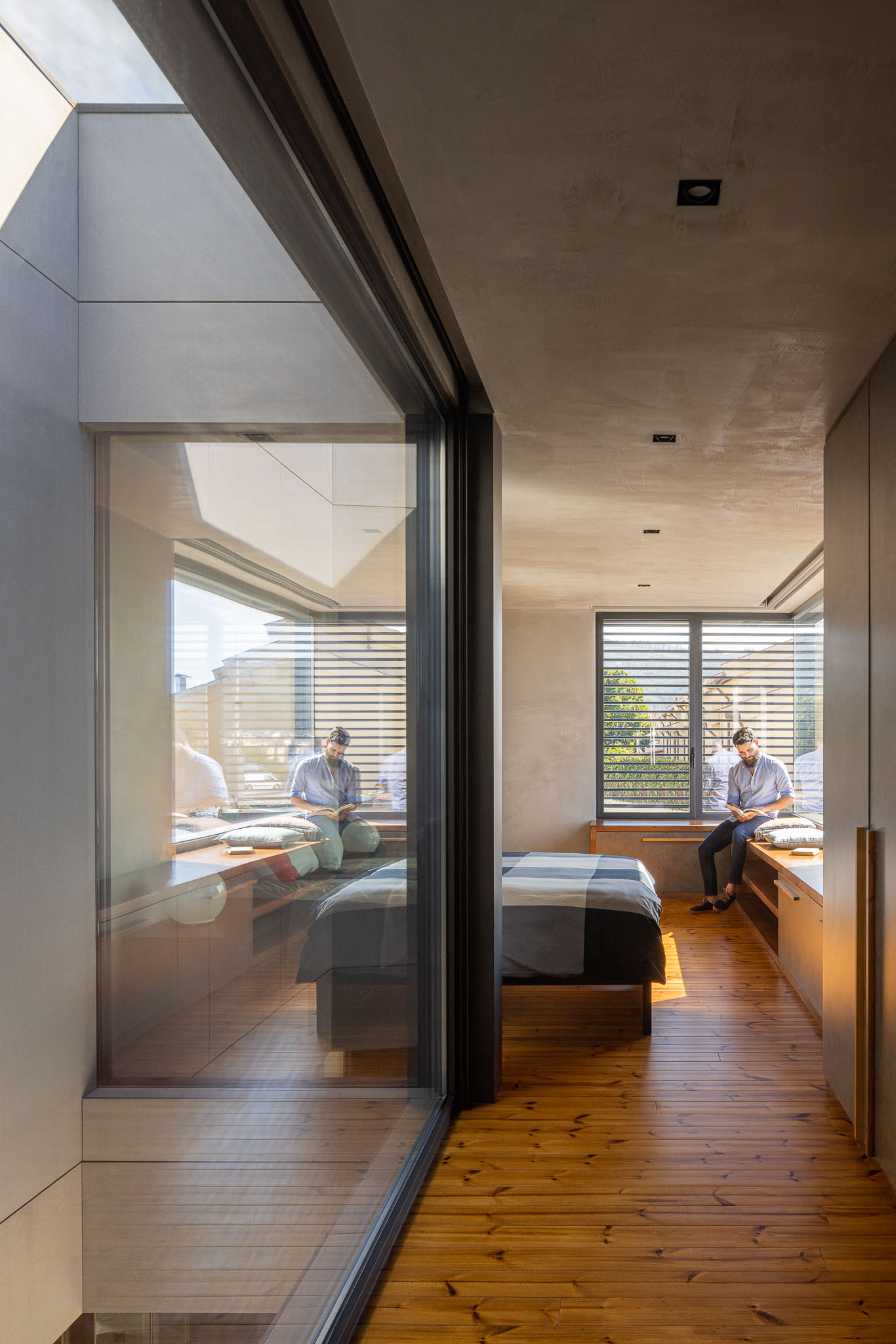 Quarto com janelas amplas, pavimento em madeira e detalhes em betão aparente. Iluminação natural. — Casa 15 arquitetura AM-arqstudio em Braga