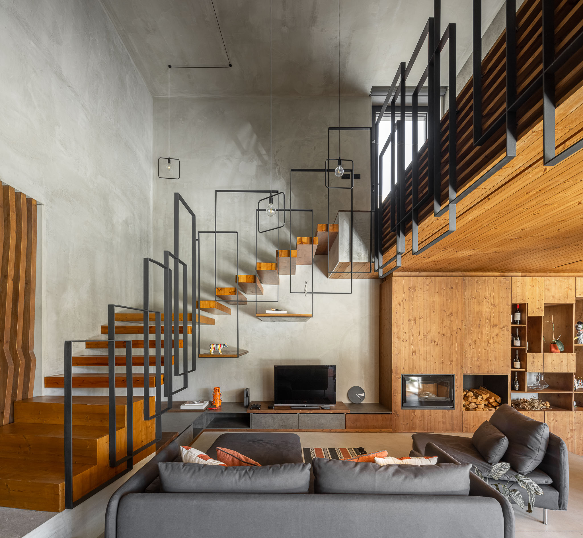 Sala de estar com escadas em madeira e metal, sofá cinzento e estante em madeira ao fundo. — Casa 15 arquitetura AM-arqstudio em Braga