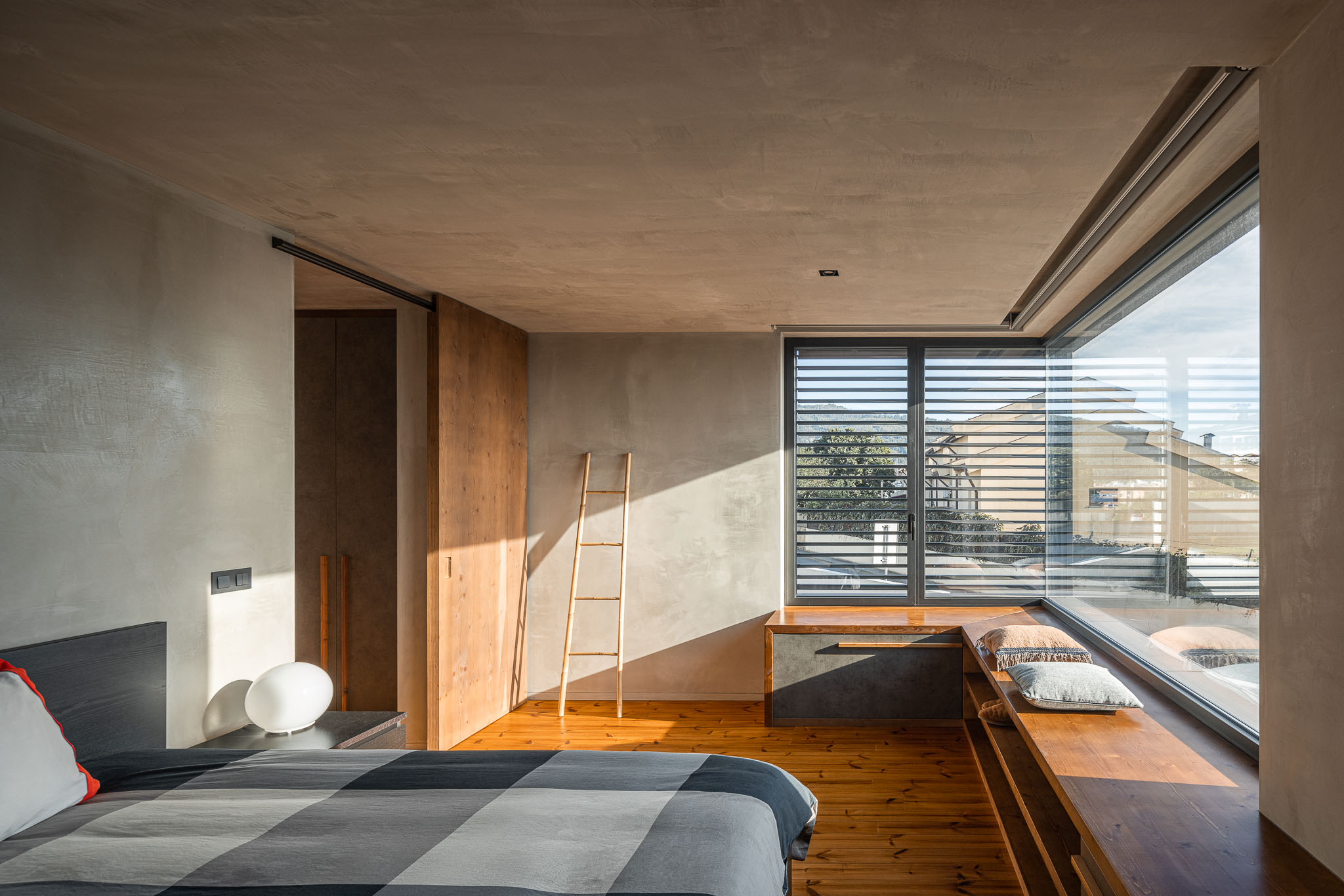 Quarto com cama, janela panorâmica com persianas e pavimento em madeira. Roupeiro em madeira. — Casa 15 arquitetura AM-arqstudio em Braga