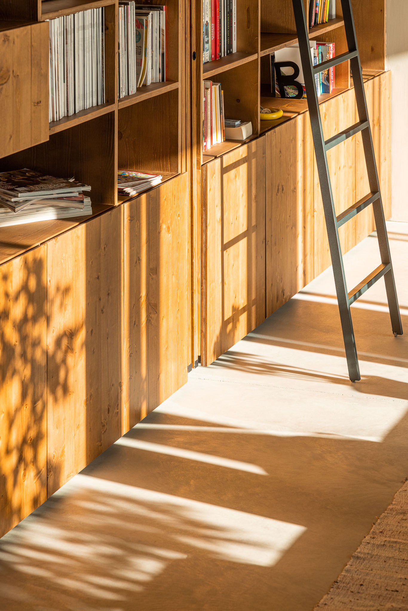 Detalhe da estante em madeira com livros e objetos decorativos, escada metálica de acesso. — Casa 15 arquitetura AM-arqstudio em Braga