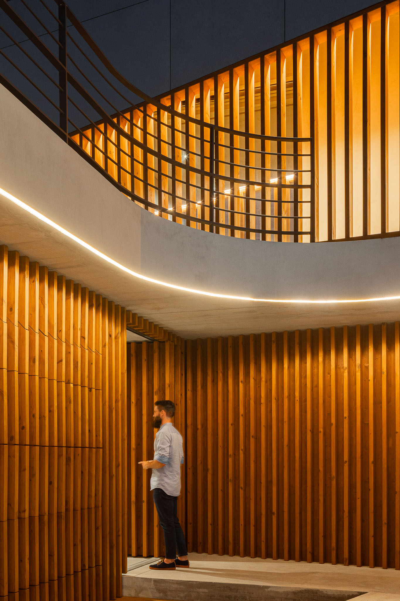Detalhe da escadaria interior com revestimento em madeira e iluminação embutida. Pessoa a subir as escadas. — Casa 15 arquitetura AM-arqstudio em Braga