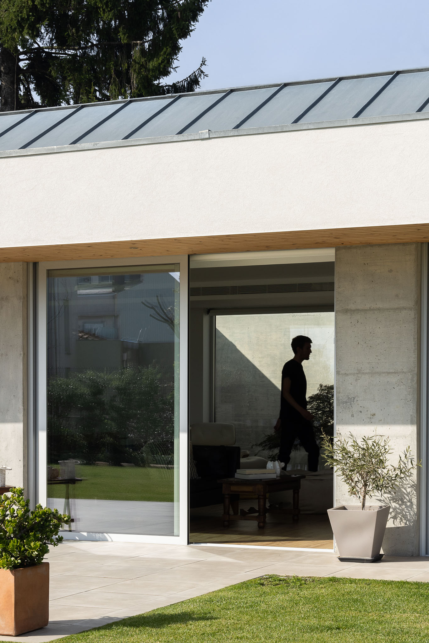 Fachada posterior com grandes janelas deslizantes, relvado e silhueta de pessoa no interior. — Casa H1 arquitetura Bruno H Gomes Arquitectura em São João da Madeira