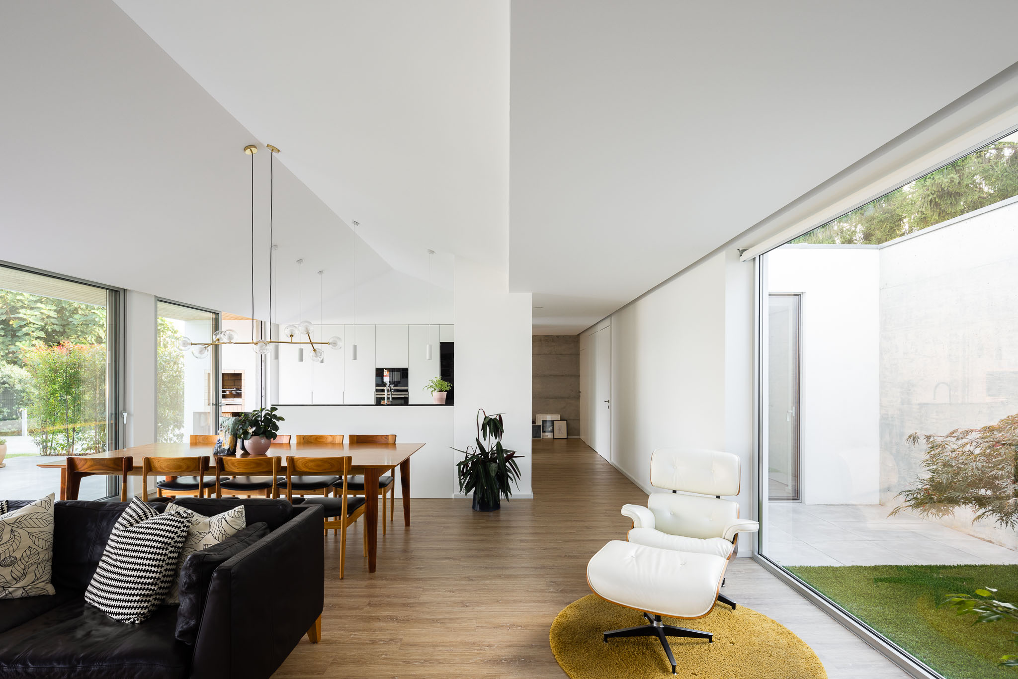 Sala de estar espaçosa com sofá preto, cadeirão branco, mesa de jantar e grandes janelas para o jardim. — Casa H1 arquitetura Bruno H Gomes Arquitectura em São João da Madeira