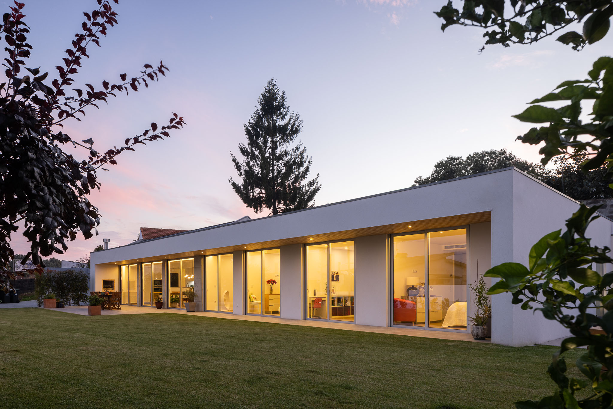 Vista exterior da casa ao entardecer, com fachada envidraçada e jardim relvado. — Casa H1 arquitetura Bruno H Gomes Arquitectura em São João da Madeira