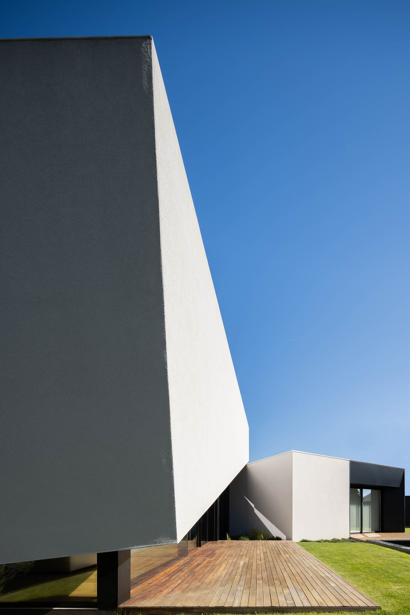 Fachada minimalista branca com detalhe em madeira e deck de madeira, sob céu azul. — Casa Tilt arquitetura Mutant Architecture and Design em Gondomar