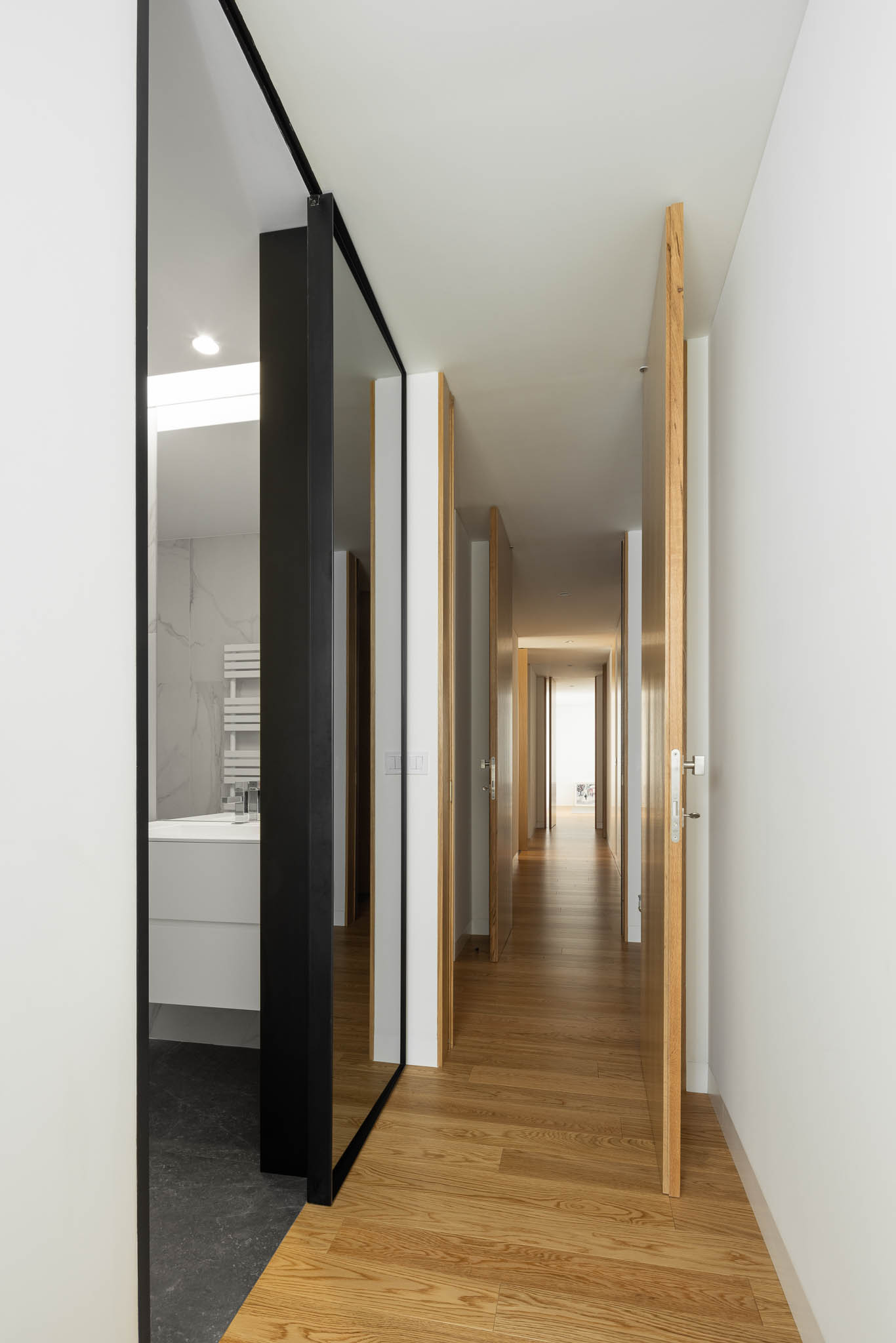 Corredor interior com pavimento em madeira, portas em madeira clara e acesso a casa de banho moderna. — Casa Tilt arquitetura Mutant Architecture and Design em Gondomar