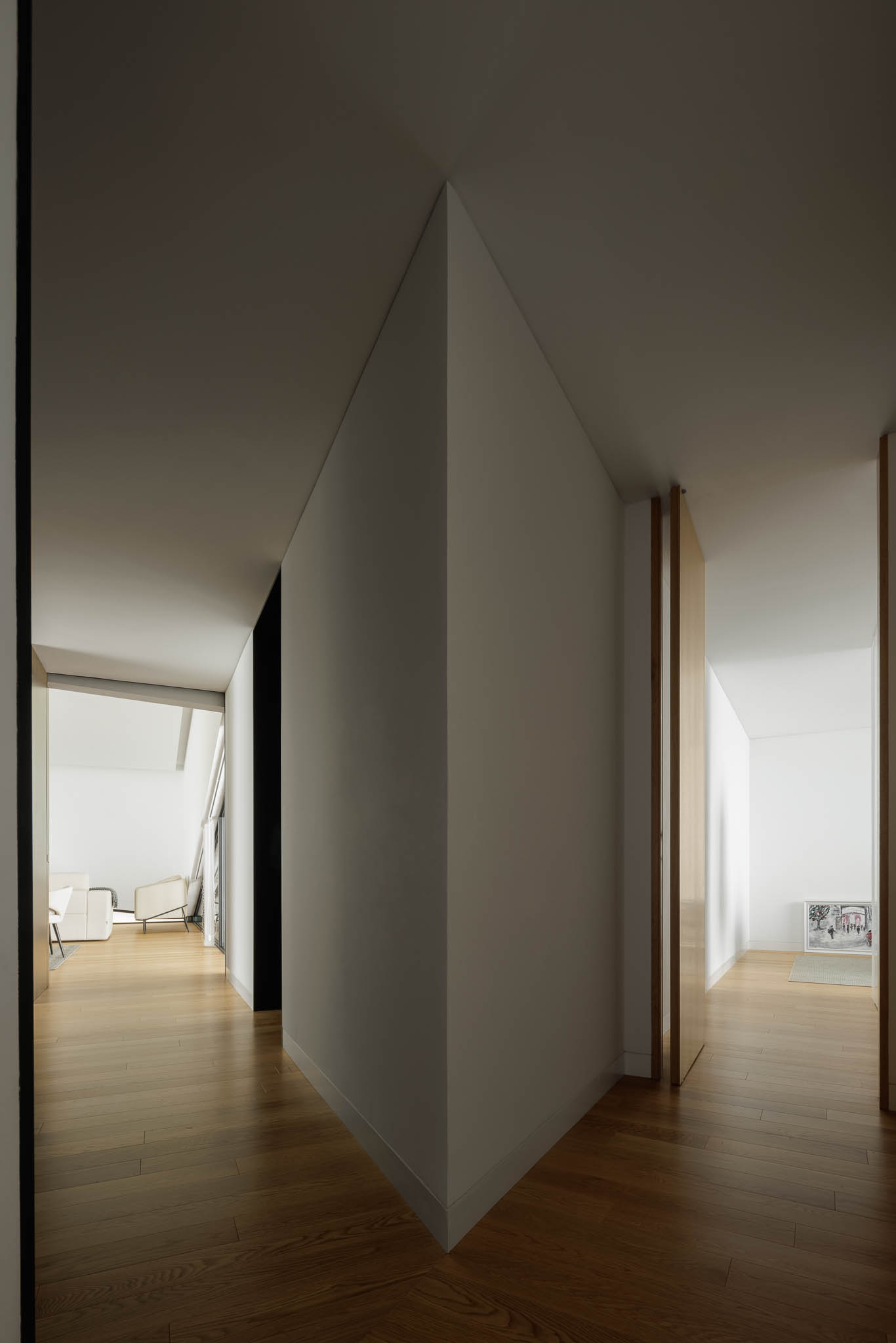 Perspectiva interior angular, corredor com pavimento em madeira, divisórias brancas e porta em madeira clara. — Casa Tilt arquitetura Mutant Architecture and Design em Gondomar