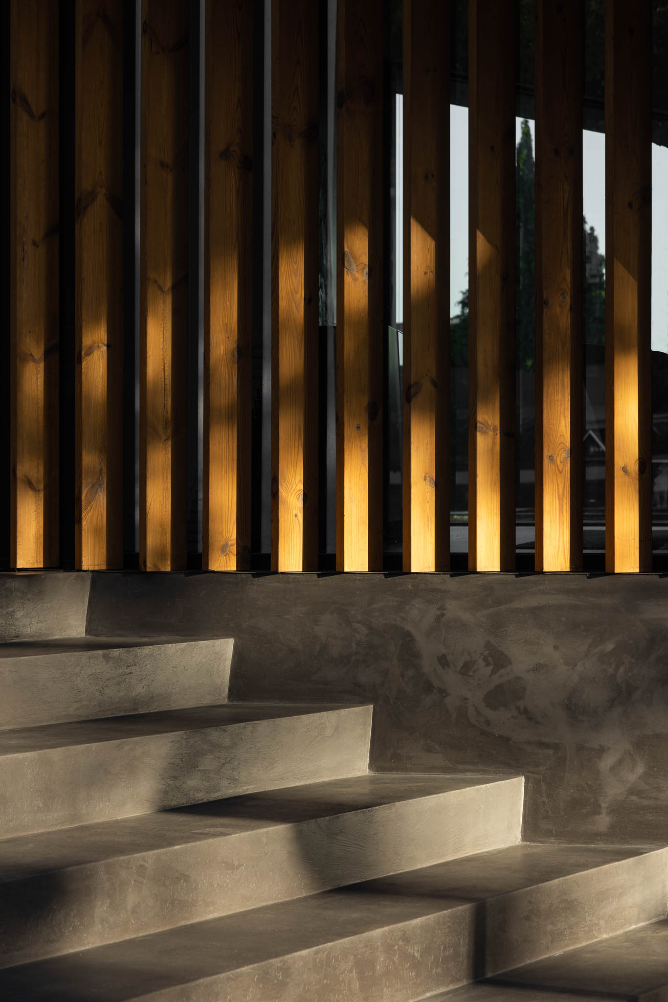 Detalhe da escadaria em betão cinzento com ripas de madeira ao fundo, com luz e sombra contrastantes. — Casa Tilt arquitetura Mutant Architecture and Design em Gondomar
