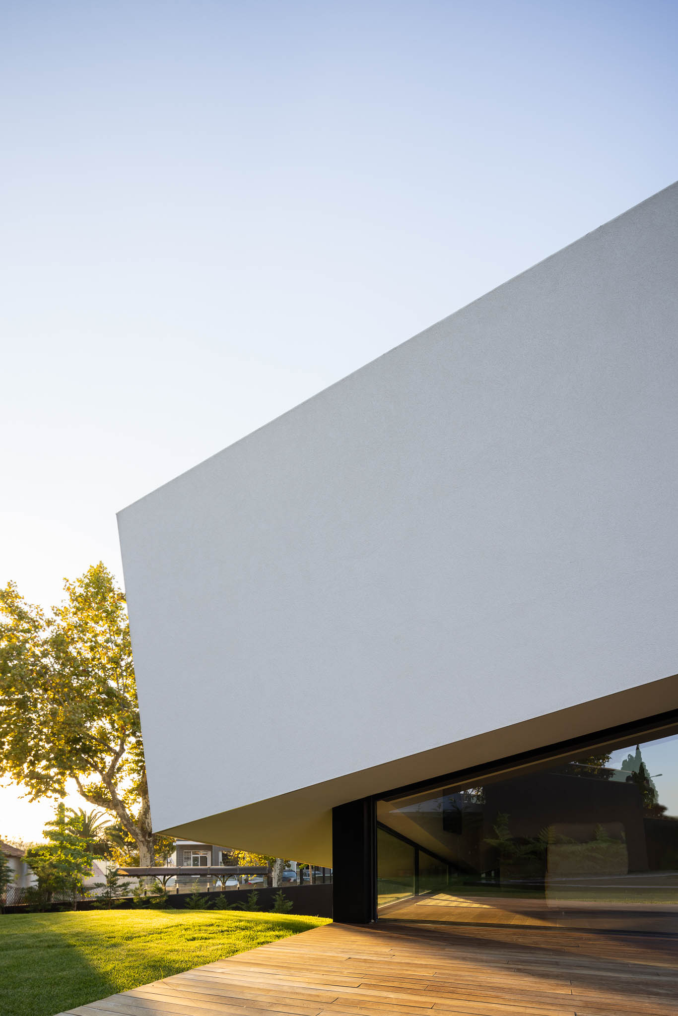 Fachada branca minimalista com janela rasgada, deck de madeira e relvado verde, sob céu claro. — Casa Tilt arquitetura Mutant Architecture and Design em Gondomar