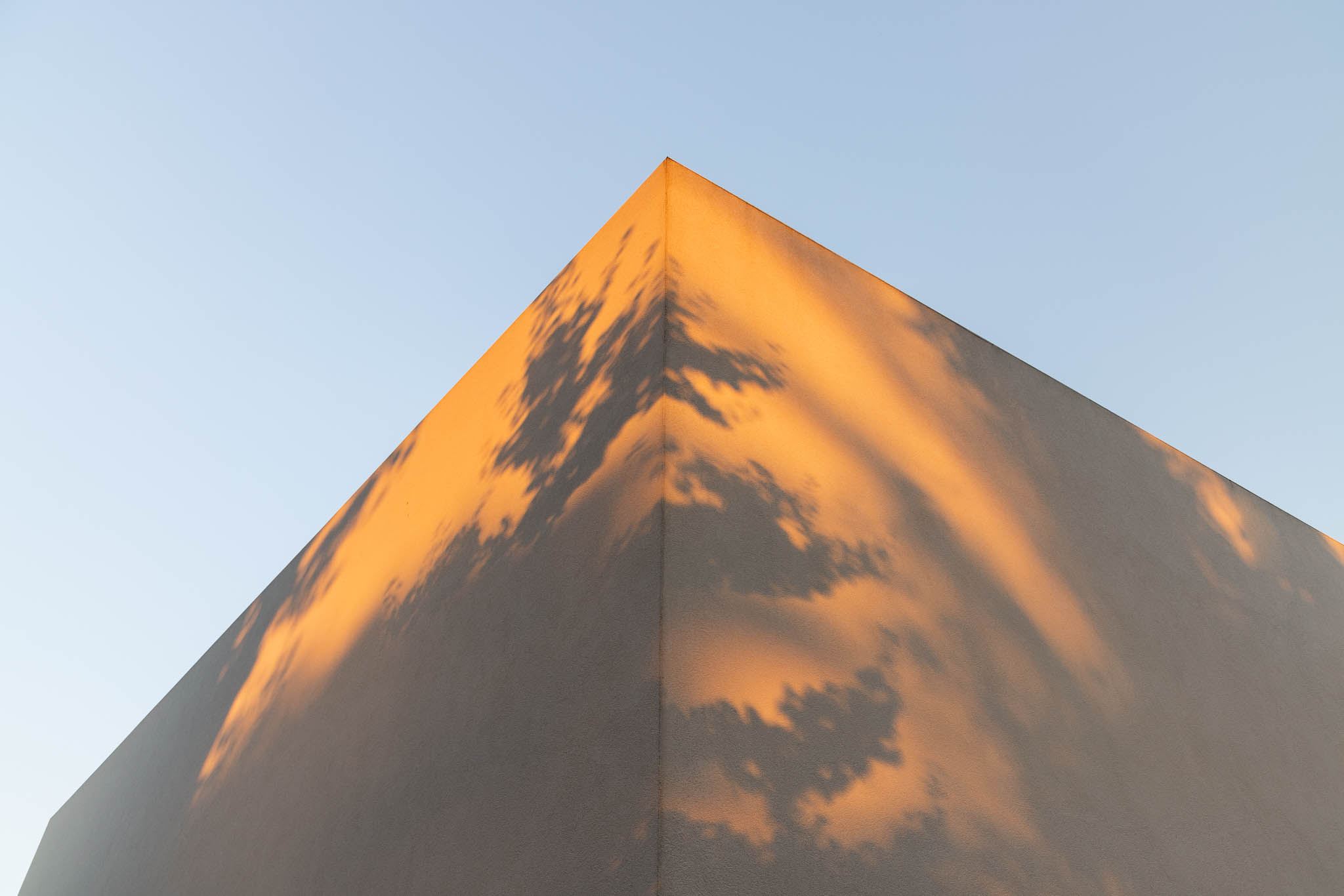 Detalhe angular da fachada branca com reflexos dourados do sol poente e sombras de nuvens. — Casa Tilt arquitetura Mutant Architecture and Design em Gondomar