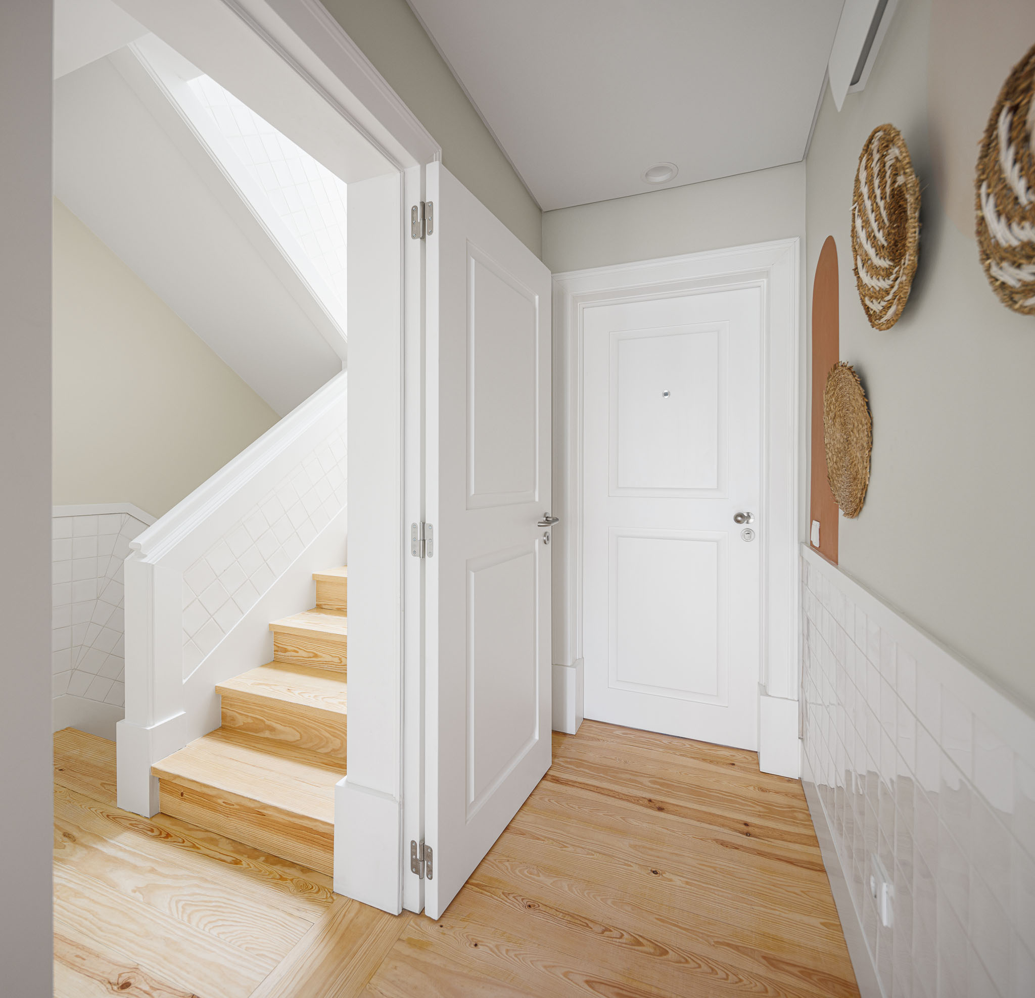 Hall de entrada com escada em madeira clara, portas brancas e parede verde-água com decoração em palha. — Graça 117 arquitetura Pedro Carrilho Arquitectos em Lisboa