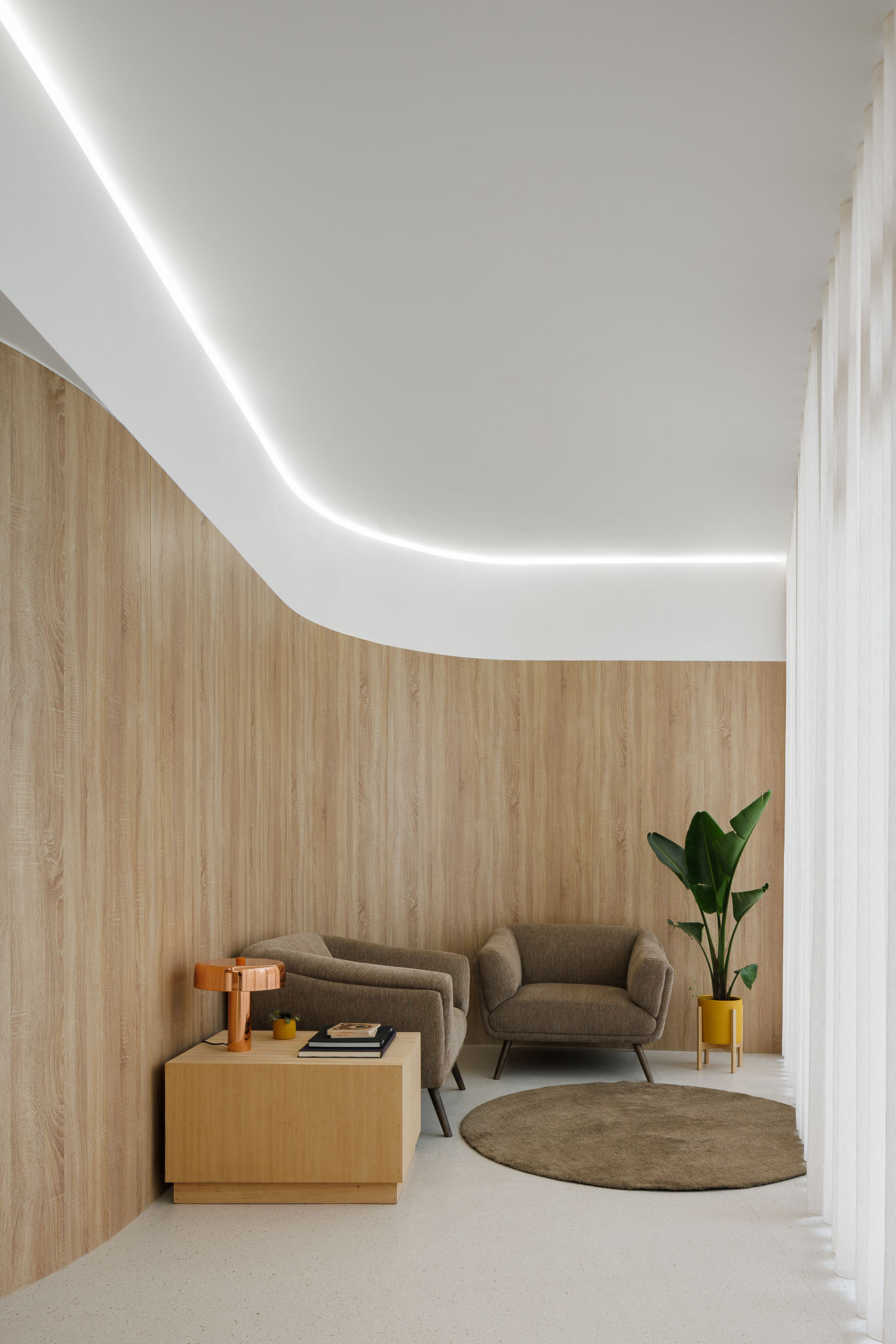 Sala de espera com cadeirões em tecido cinza, mesa lateral em madeira clara e iluminação indireta linear. — MOOD Medicina Dentária arquitetura Tsou Arquitectos em Maia