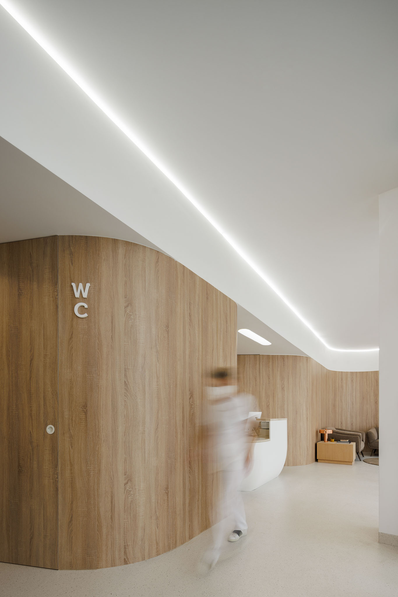 Corredor curvo com revestimento em madeira e sinalização WC, pavimento em terrazzo claro. — MOOD Medicina Dentária arquitetura Tsou Arquitectos em Maia