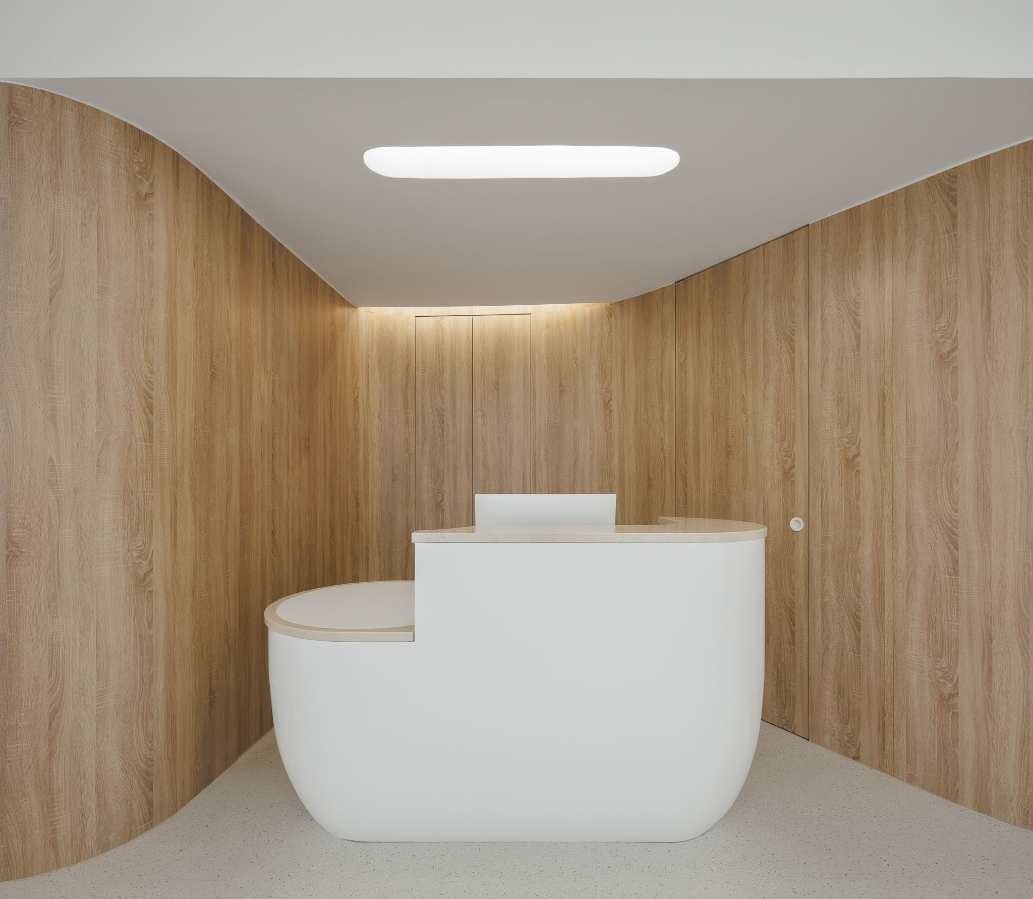 Balcão de receção branco com design orgânico, em ambiente revestido a madeira clara. — MOOD Medicina Dentária arquitetura Tsou Arquitectos em Maia