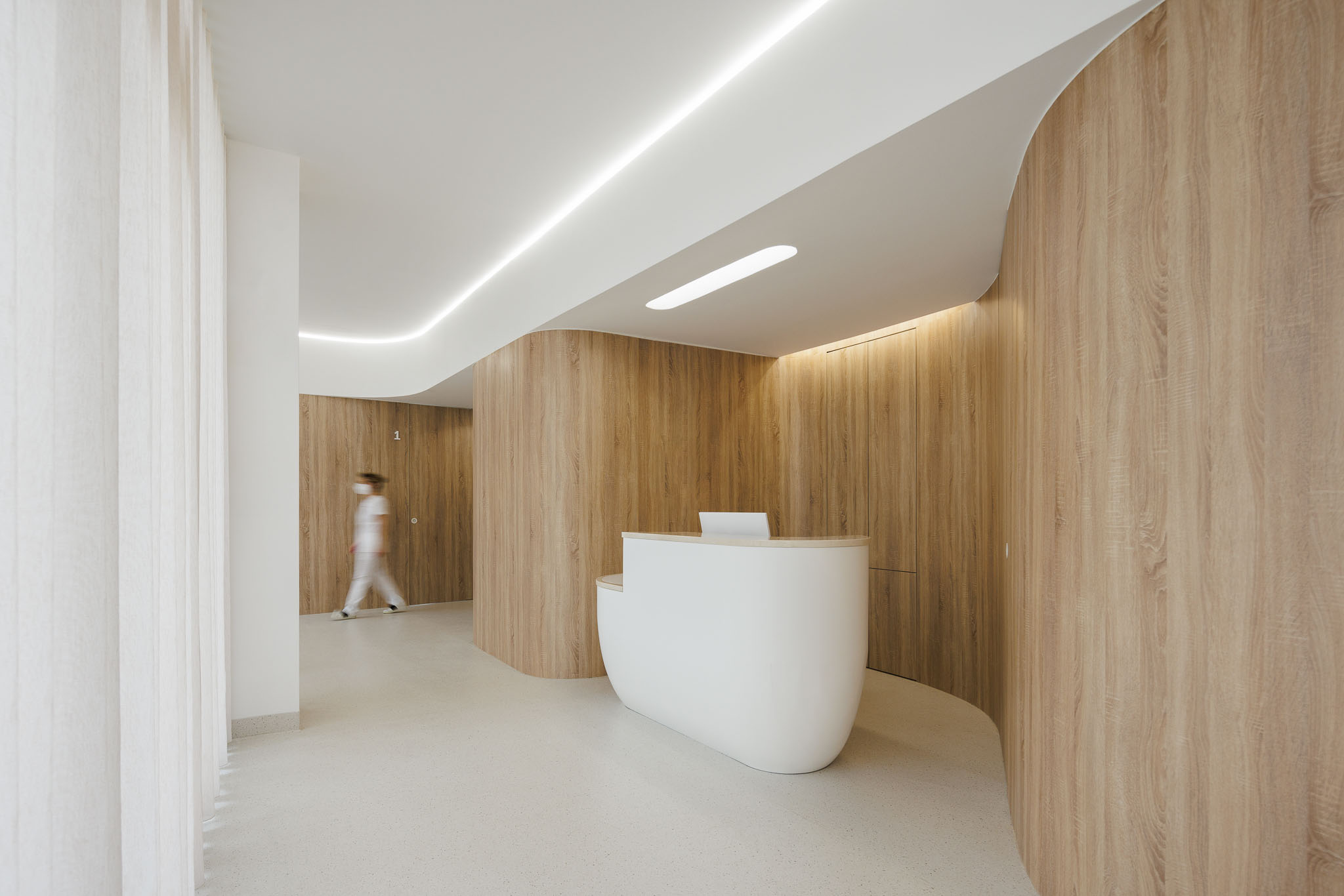 Entrada da clínica com balcão branco, corredor curvo em madeira e cortinas translúcidas. — MOOD Medicina Dentária arquitetura Tsou Arquitectos em Maia