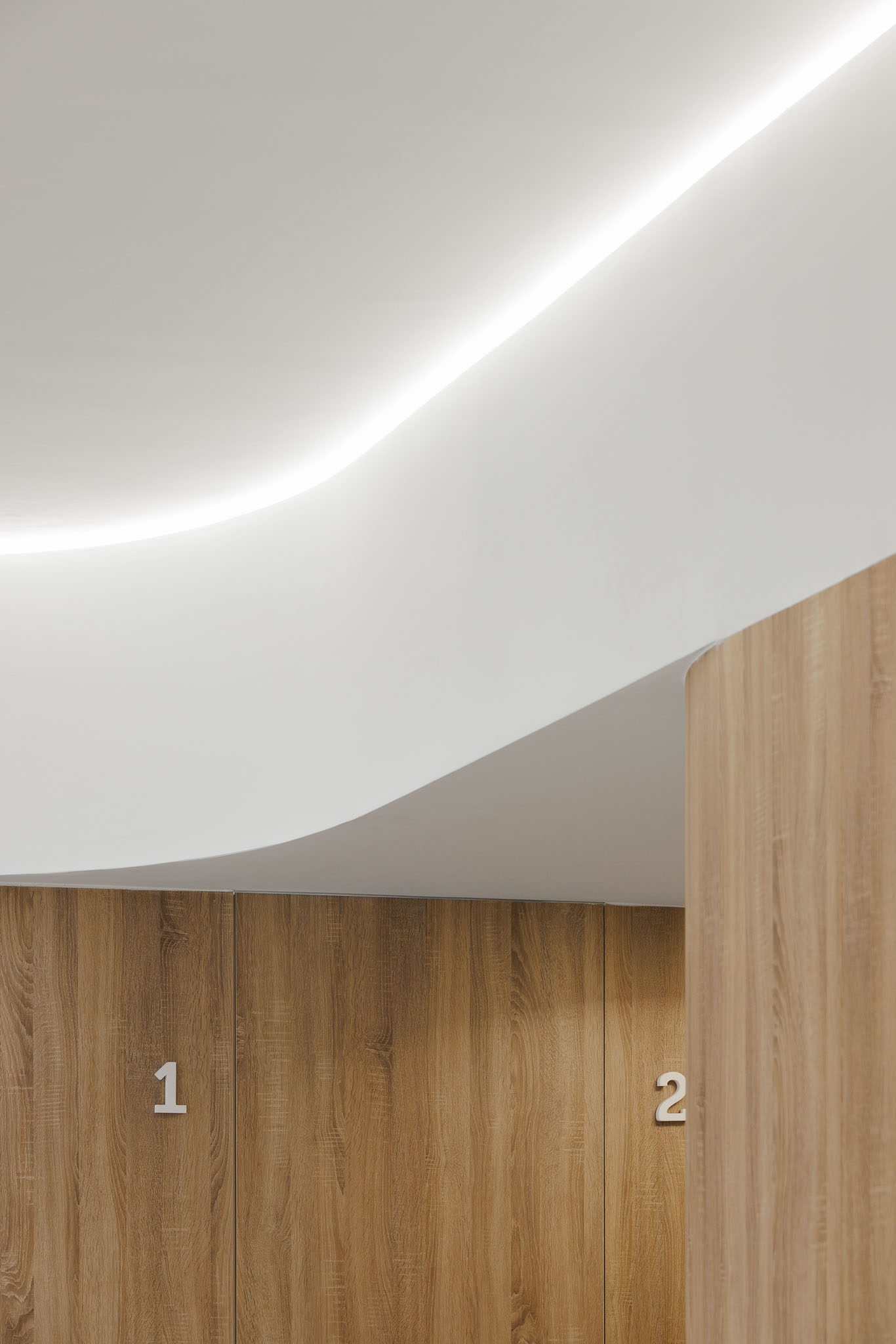 Detalhe do corredor com portas em madeira, números em branco e teto curvo com luz indireta. — MOOD Medicina Dentária arquitetura Tsou Arquitectos em Maia