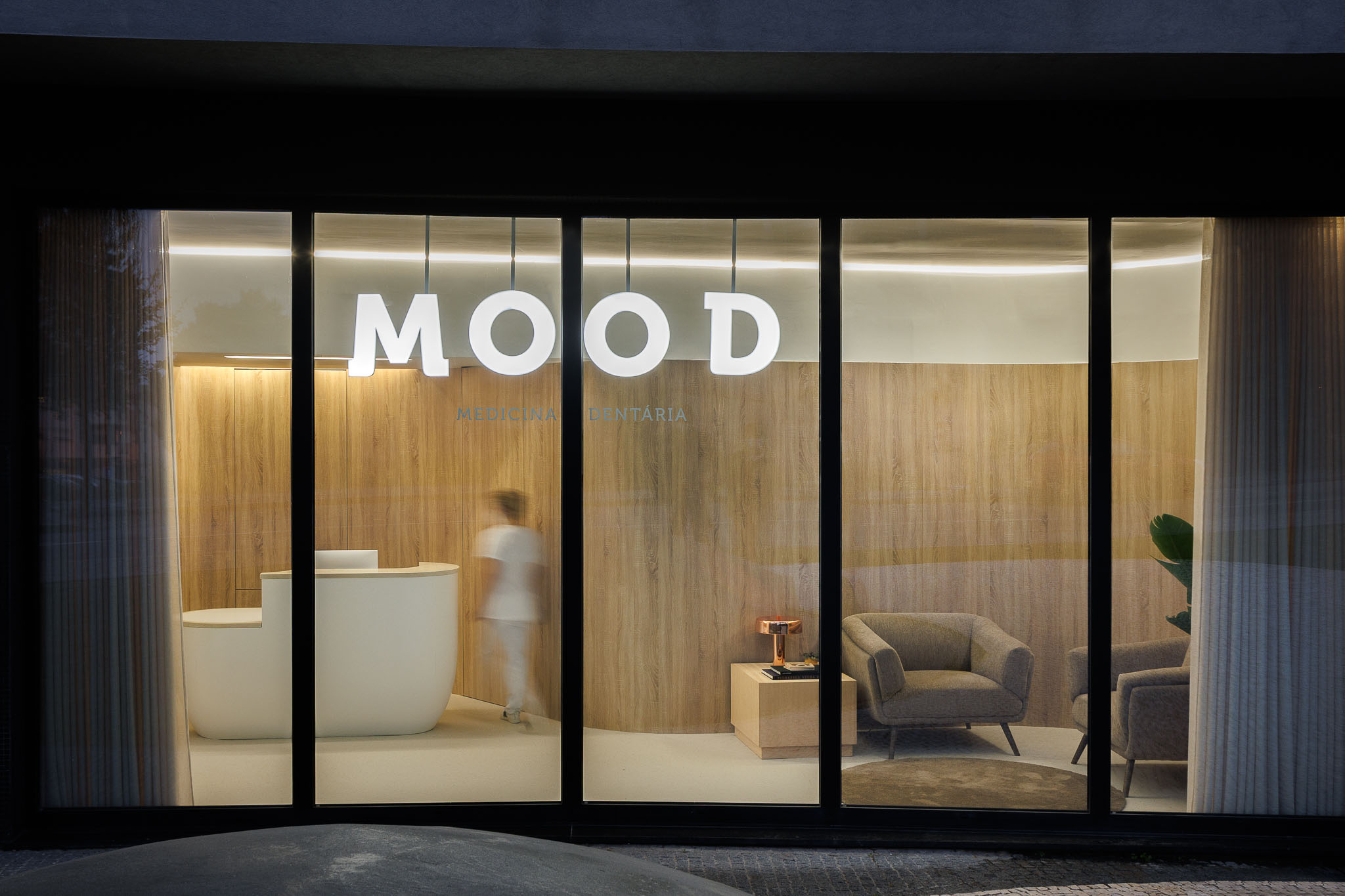 Fachada noturna da clínica com o nome "MOOD" em destaque, interior com receção e sala de espera. — MOOD Medicina Dentária arquitetura Tsou Arquitectos em Maia