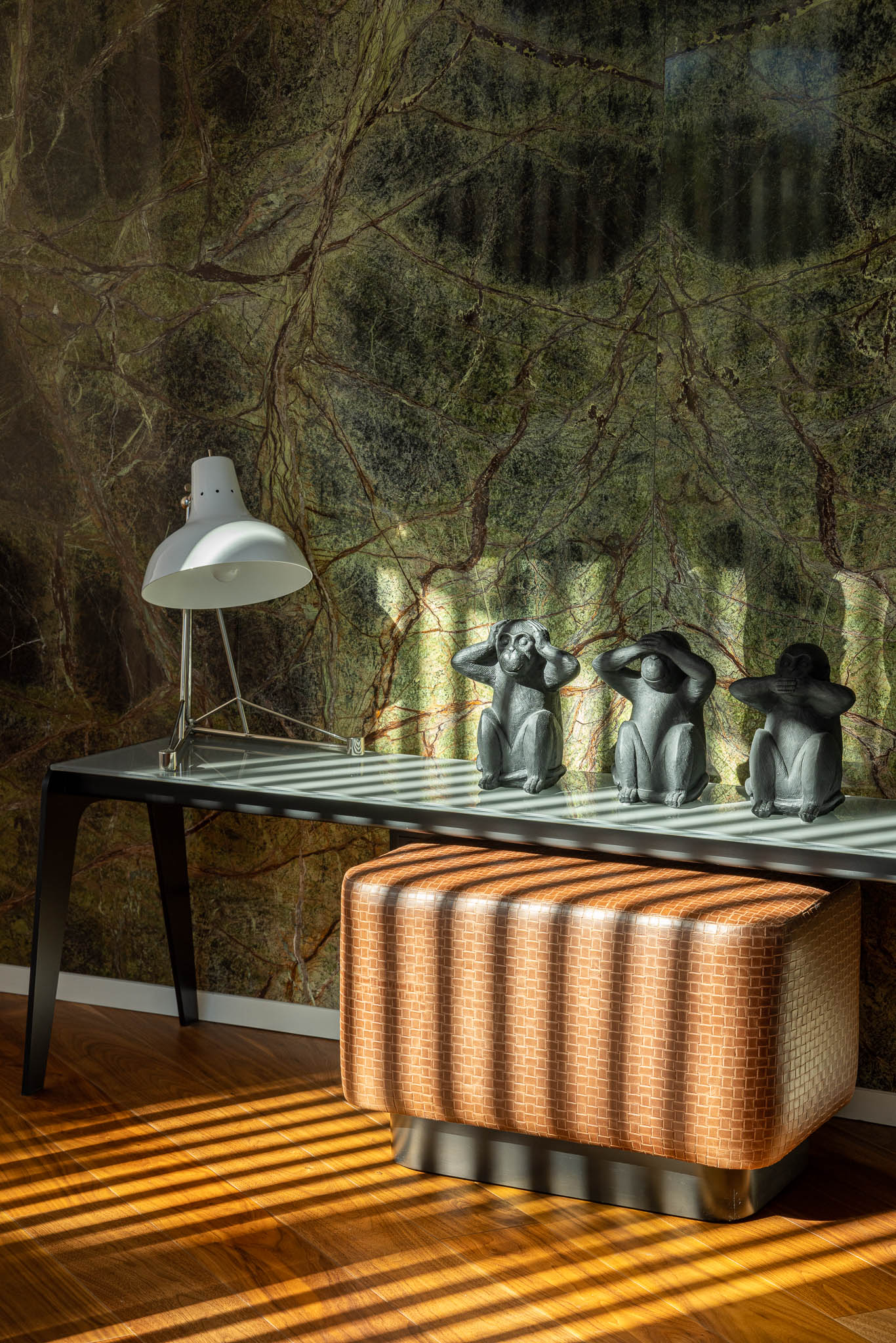 Detalhe da consola com estatuetas, candeeiro e pufe em frente à parede de mármore verde com veios marcantes. — Casa PS arquitetura Inception Architects Studio em Braga