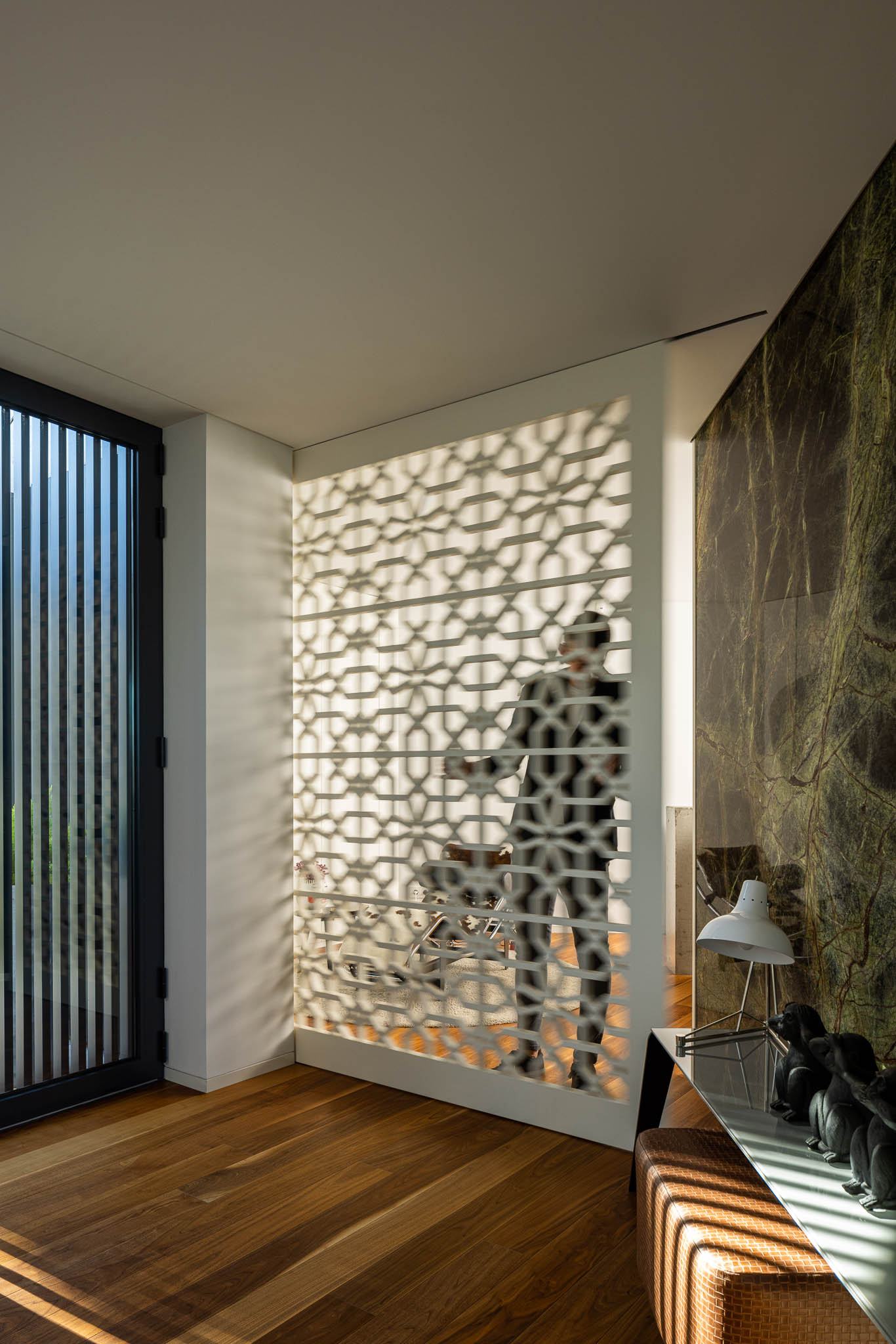 Hall com biombo rendilhado branco, porta de acesso e parede em mármore verde, com luz natural rasante no pavimento. — Casa PS arquitetura Inception Architects Studio em Braga