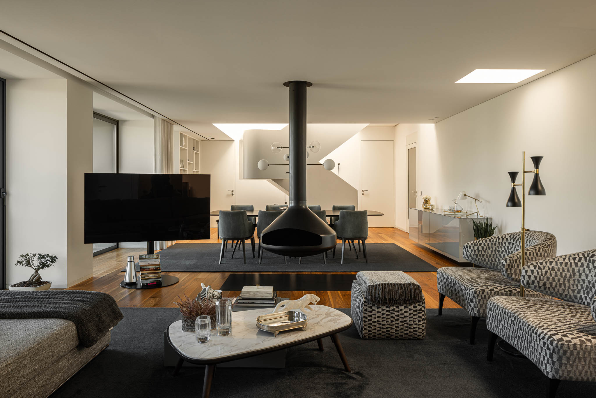 Sala de estar ampla com lareira suspensa, sofás e cadeirões modernos, tapete escuro e pavimento em madeira. — Casa PS arquitetura Inception Architects Studio em Braga