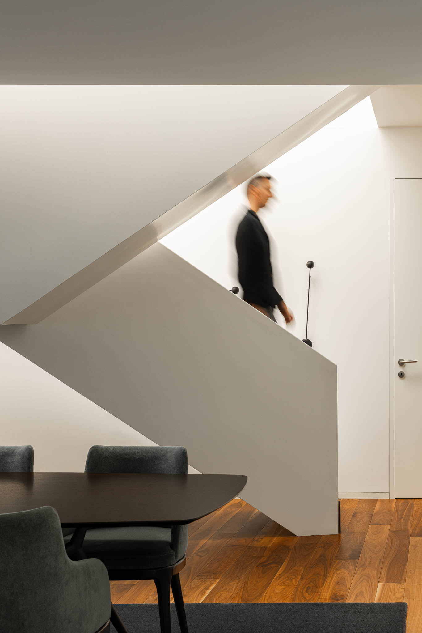 Escada minimalista com corrimão metálico, paredes brancas e pavimento em madeira, com luz zenital. — Casa PS arquitetura Inception Architects Studio em Braga