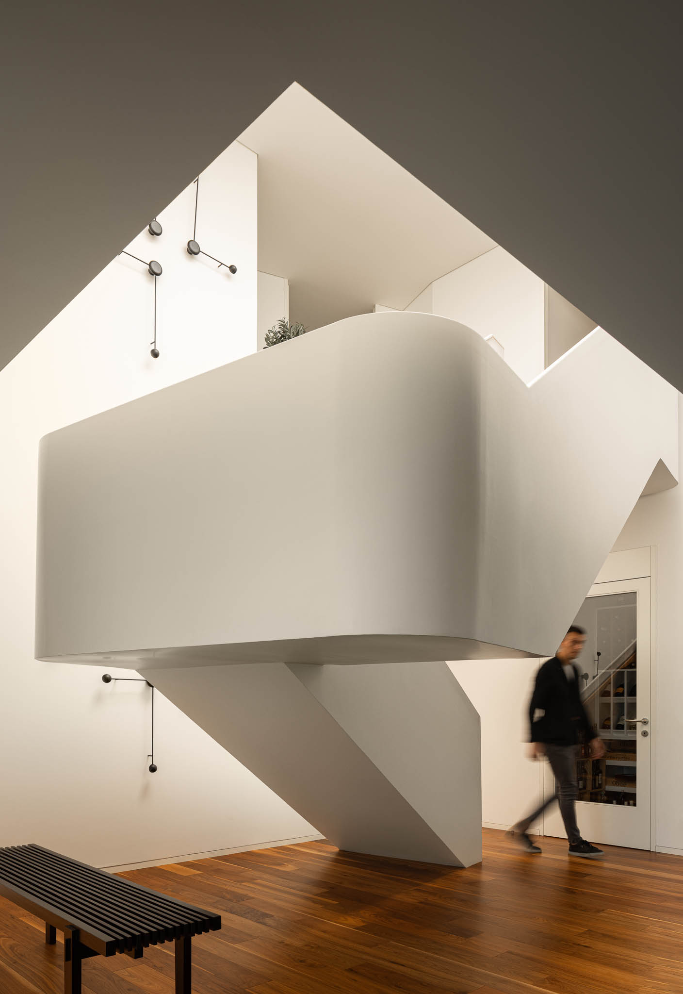 Escada suspensa com design arrojado, paredes brancas, pavimento em madeira e banco preto de ripas. — Casa PS arquitetura Inception Architects Studio em Braga