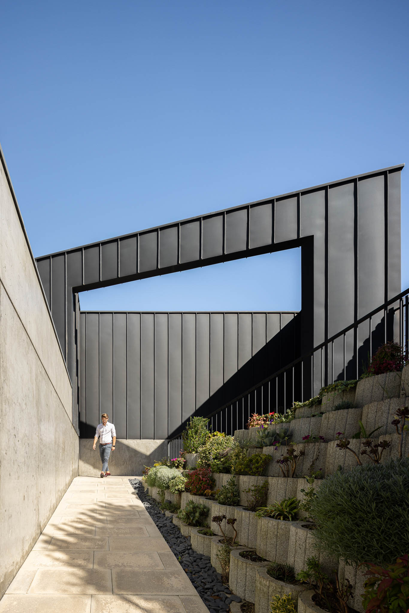 Exterior da casa com jardim em socalcos, revestimento em zinco preto e parede em betão aparente. — Casa PS arquitetura Inception Architects Studio em Braga