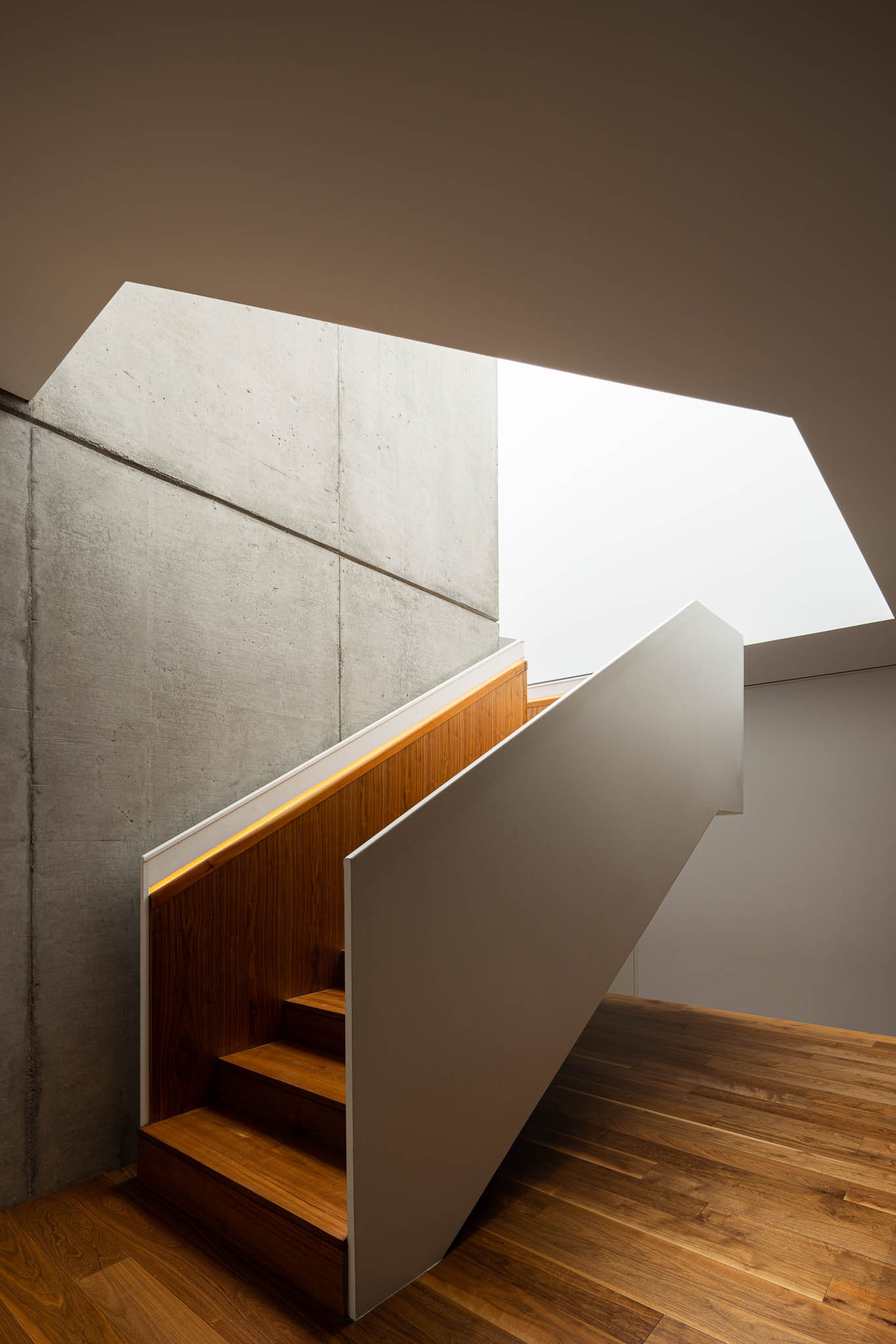 Detalhe da escada com degraus em madeira, parede em betão aparente e iluminação embutida. — Casa PS arquitetura Inception Architects Studio em Braga