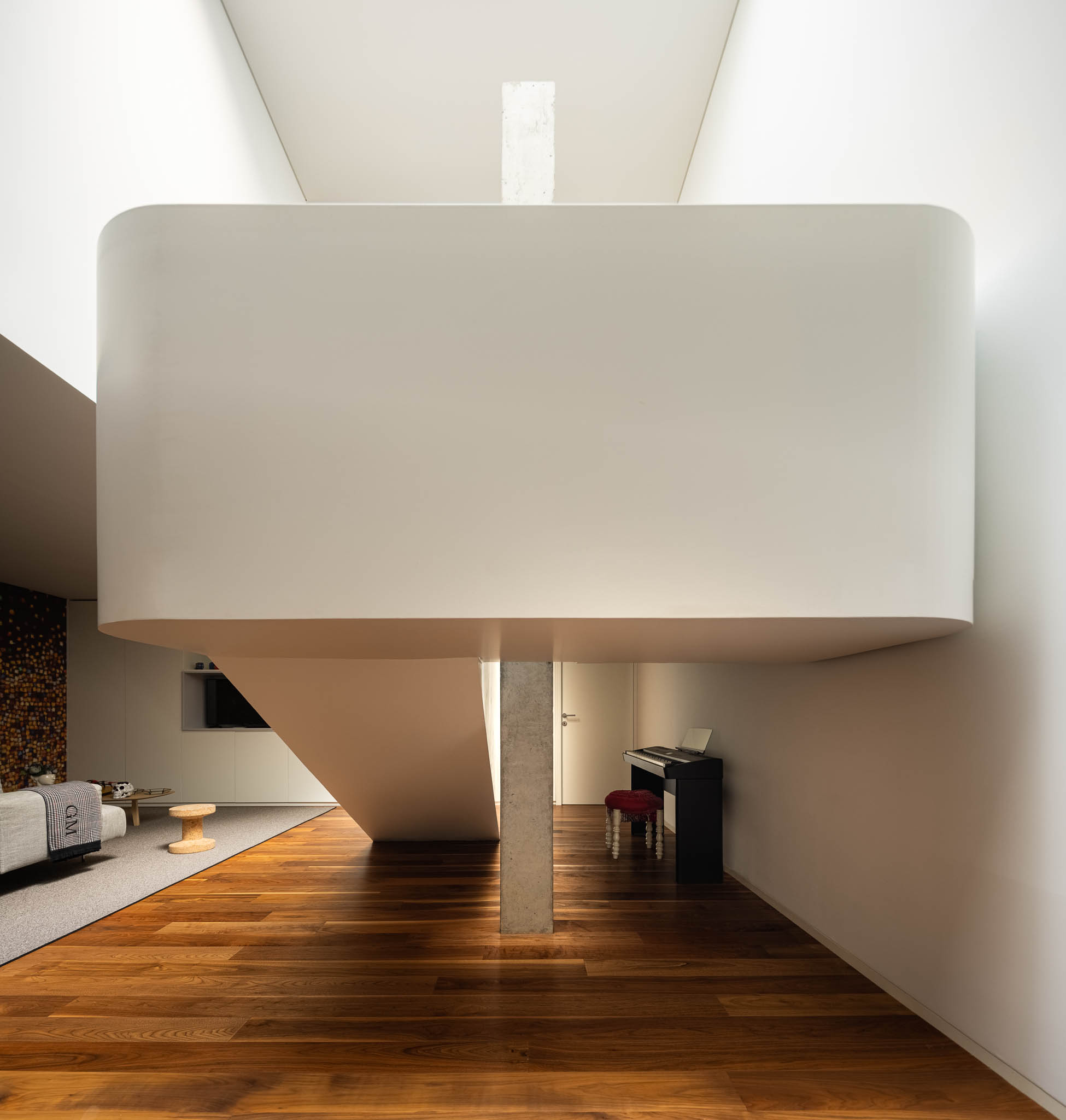 Espaço interior com escada suspensa, pilar de suporte em betão, piano e zona de estar ao fundo. — Casa PS arquitetura Inception Architects Studio em Braga