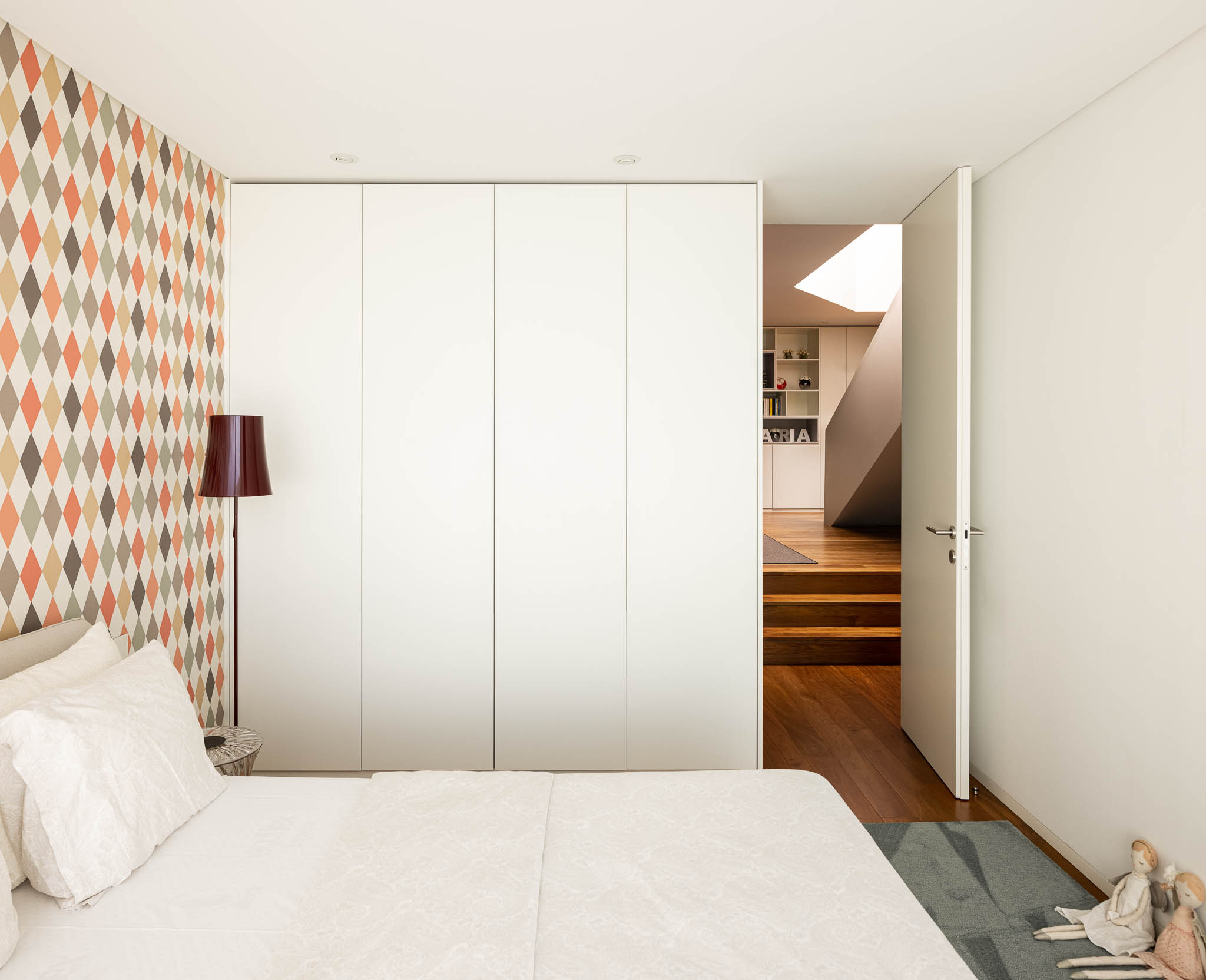 Quarto com papel de parede geométrico, armário branco embutido e acesso à escada em madeira. — Casa PS arquitetura Inception Architects Studio em Braga