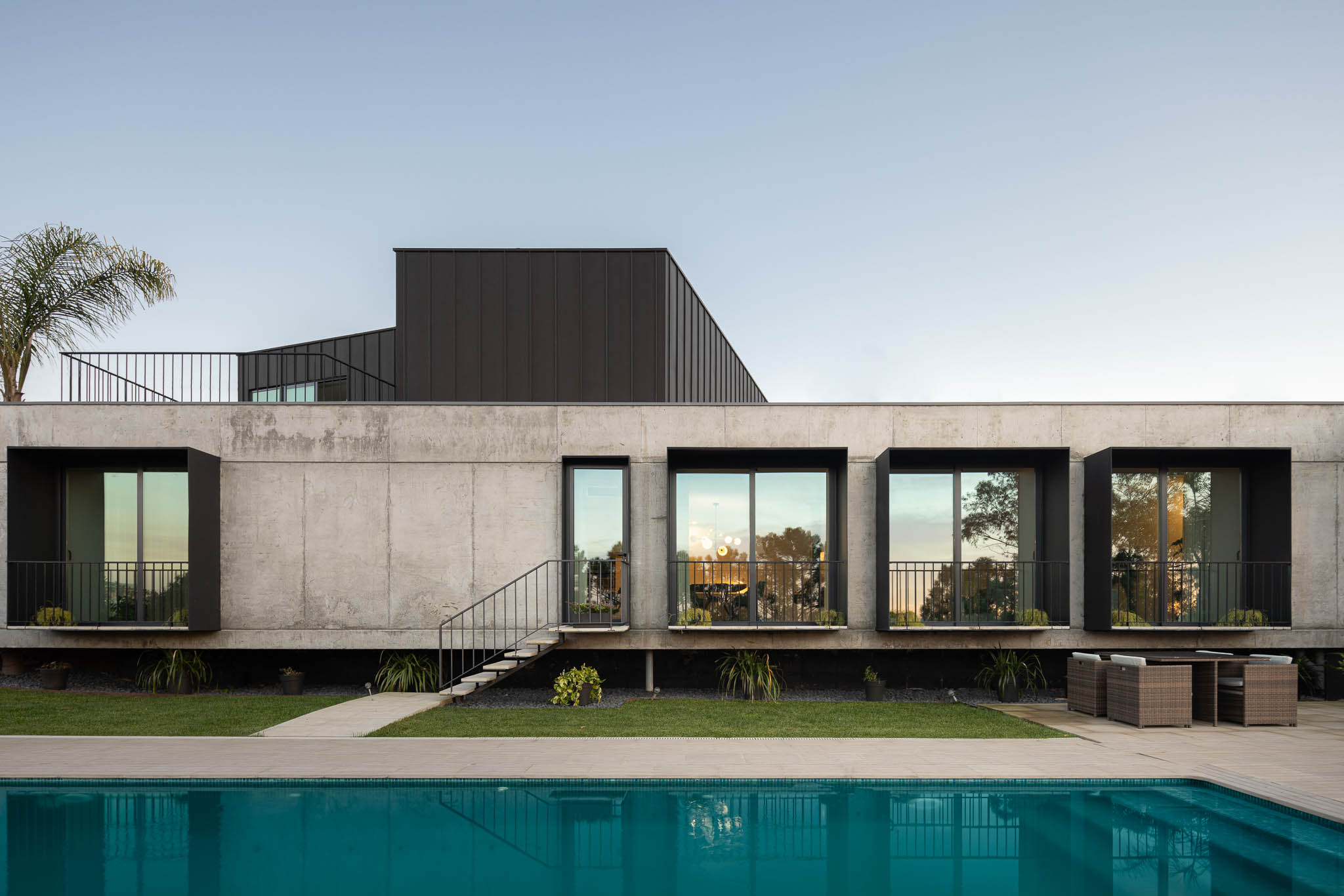 Fachada da casa com piscina, janelas emolduradas a preto, revestimento em betão e jardim relvado. — Casa PS arquitetura Inception Architects Studio em Braga