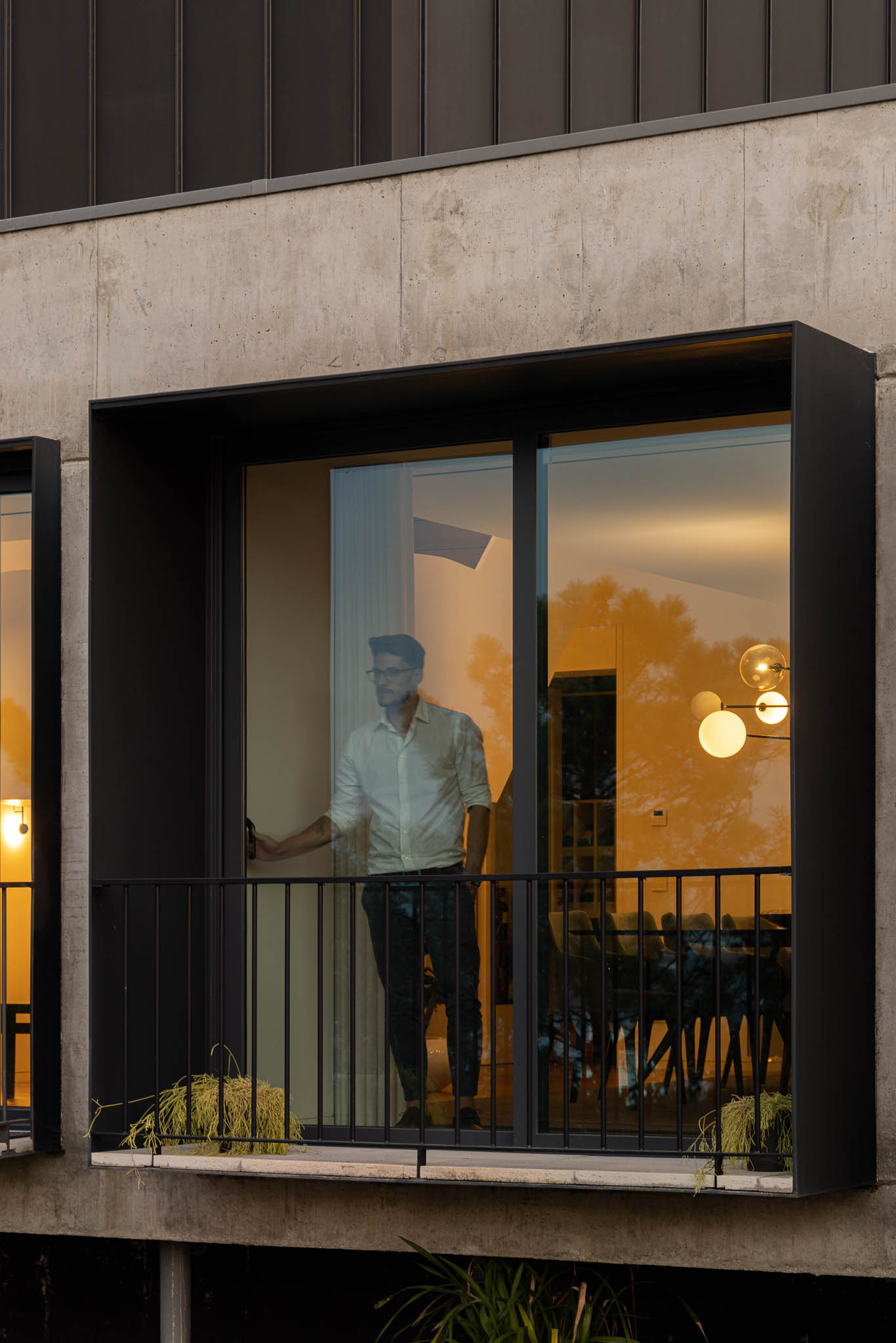 Detalhe da janela com moldura preta, varanda com gradeamento e pessoa a observar o interior da casa. — Casa PS arquitetura Inception Architects Studio em Braga