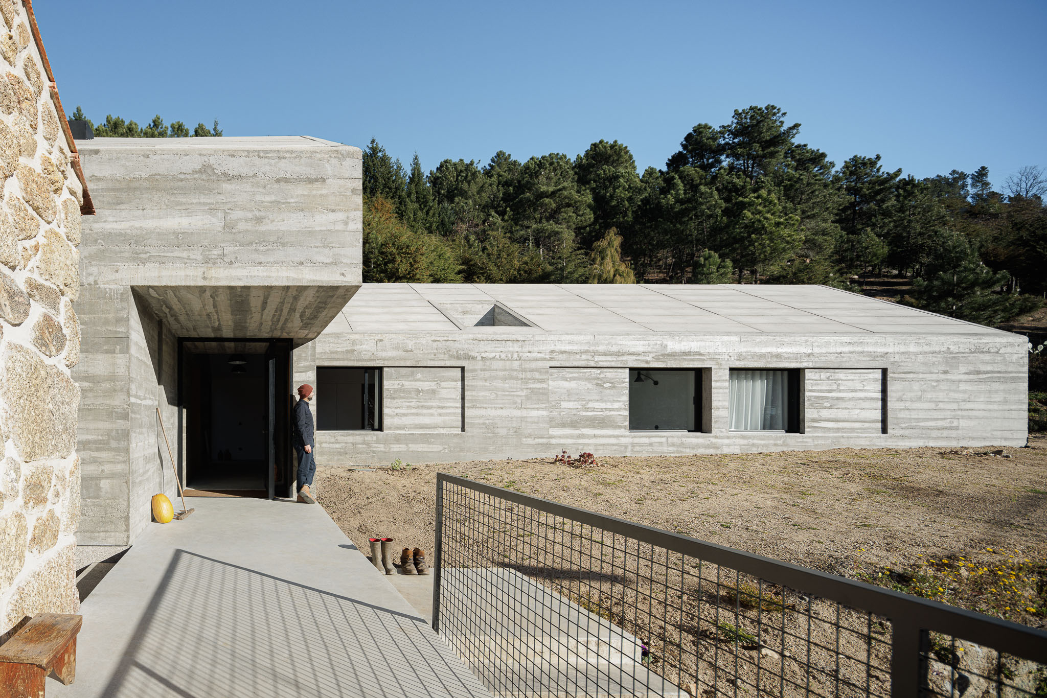 Casa NaMora: Fachada em betão aparente, linhas retas, anexo em pedra, passadiço metálico e paisagem natural. — Casa NaMora arquitetura David Bilo Arquitectos e Filipe Pina Arquitectura em Guarda