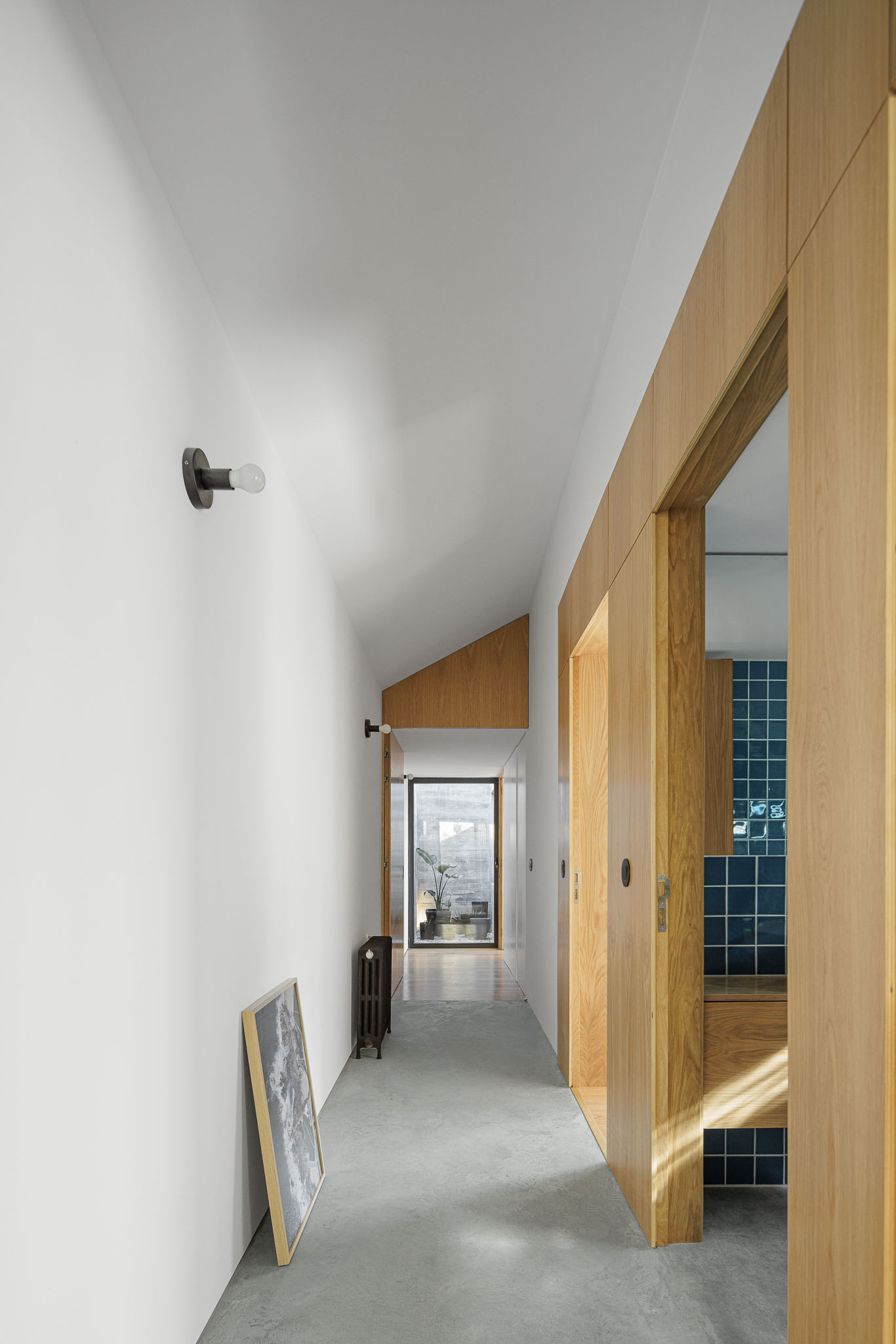 Casa NaMora: Corredor interior com paredes brancas, detalhes em madeira clara e pavimento em cimento afagado. — Casa NaMora arquitetura David Bilo Arquitectos e Filipe Pina Arquitectura em Guarda