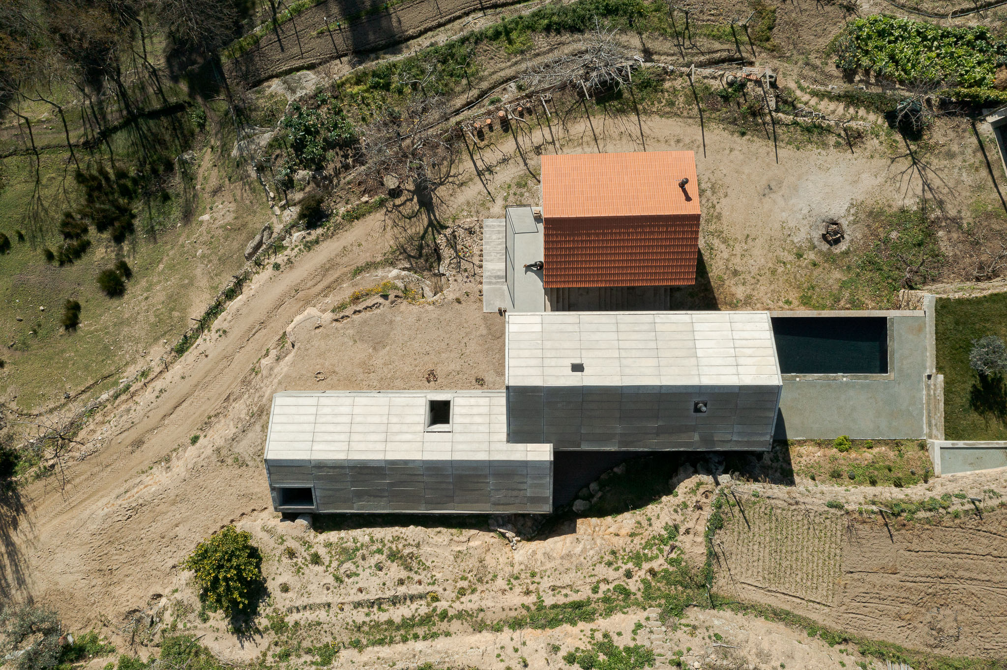 Casa NaMora: Vista aérea da casa com telhado cerâmico, piscina e anexo em betão, inserida num terreno acidentado. — Casa NaMora arquitetura David Bilo Arquitectos e Filipe Pina Arquitectura em Guarda