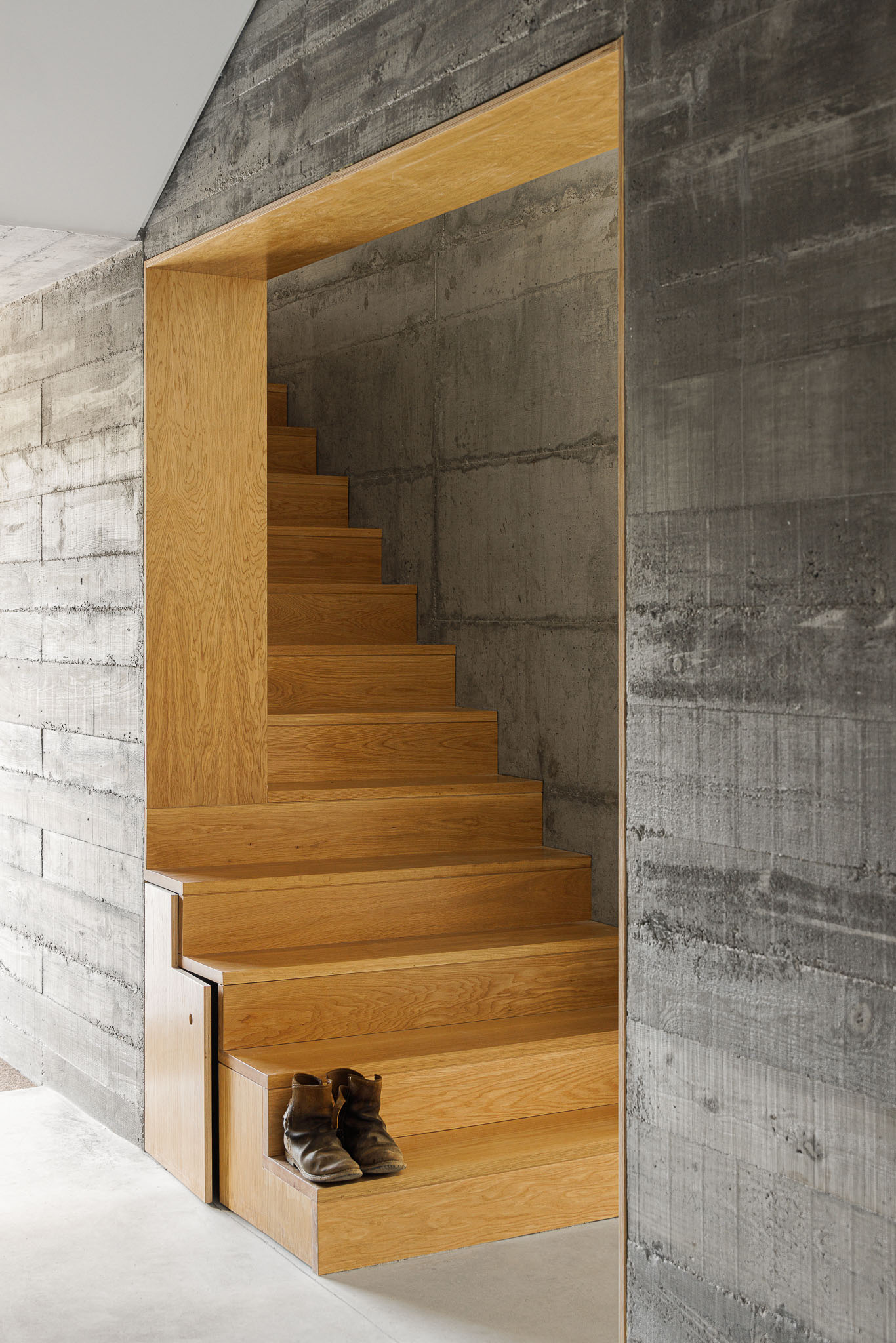 Casa NaMora: Escadas em madeira clara contrastando com paredes em betão aparente, criando um ambiente rústico e moderno. — Casa NaMora arquitetura David Bilo Arquitectos e Filipe Pina Arquitectura em Guarda