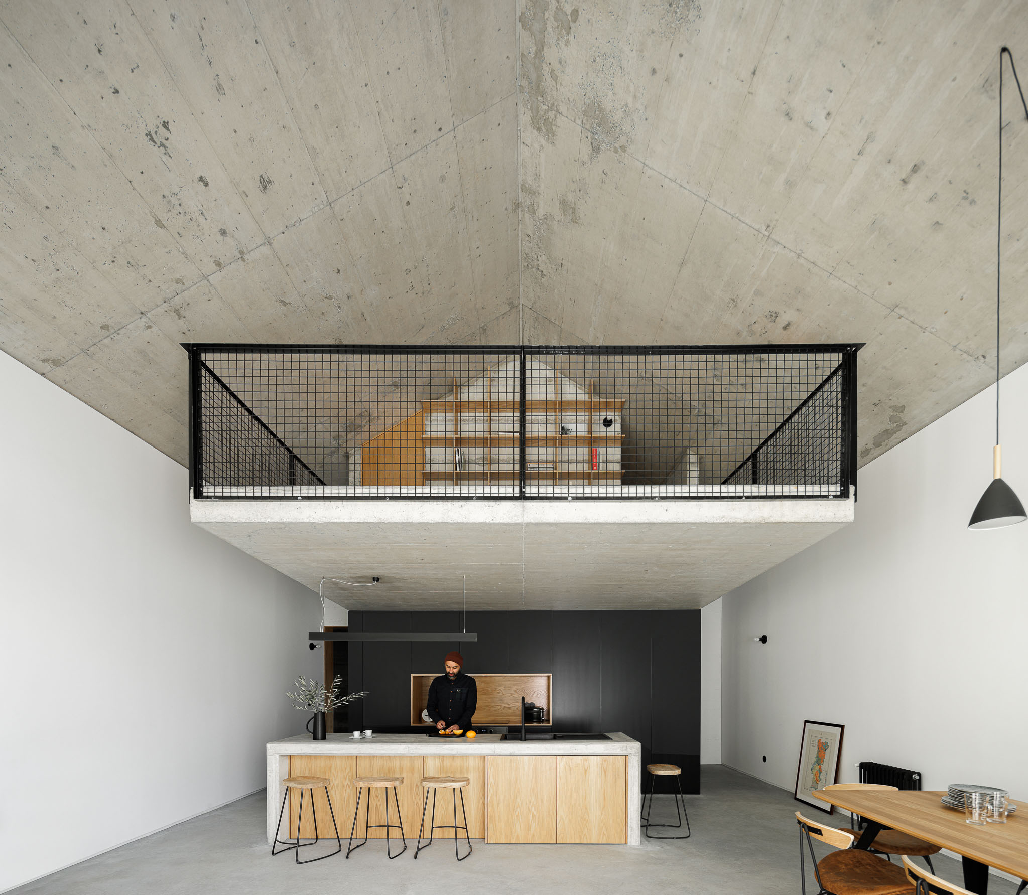 Casa NaMora: Interior amplo com cozinha em ilha, mezanino com grade metálica e teto em betão aparente. — Casa NaMora arquitetura David Bilo Arquitectos e Filipe Pina Arquitectura em Guarda